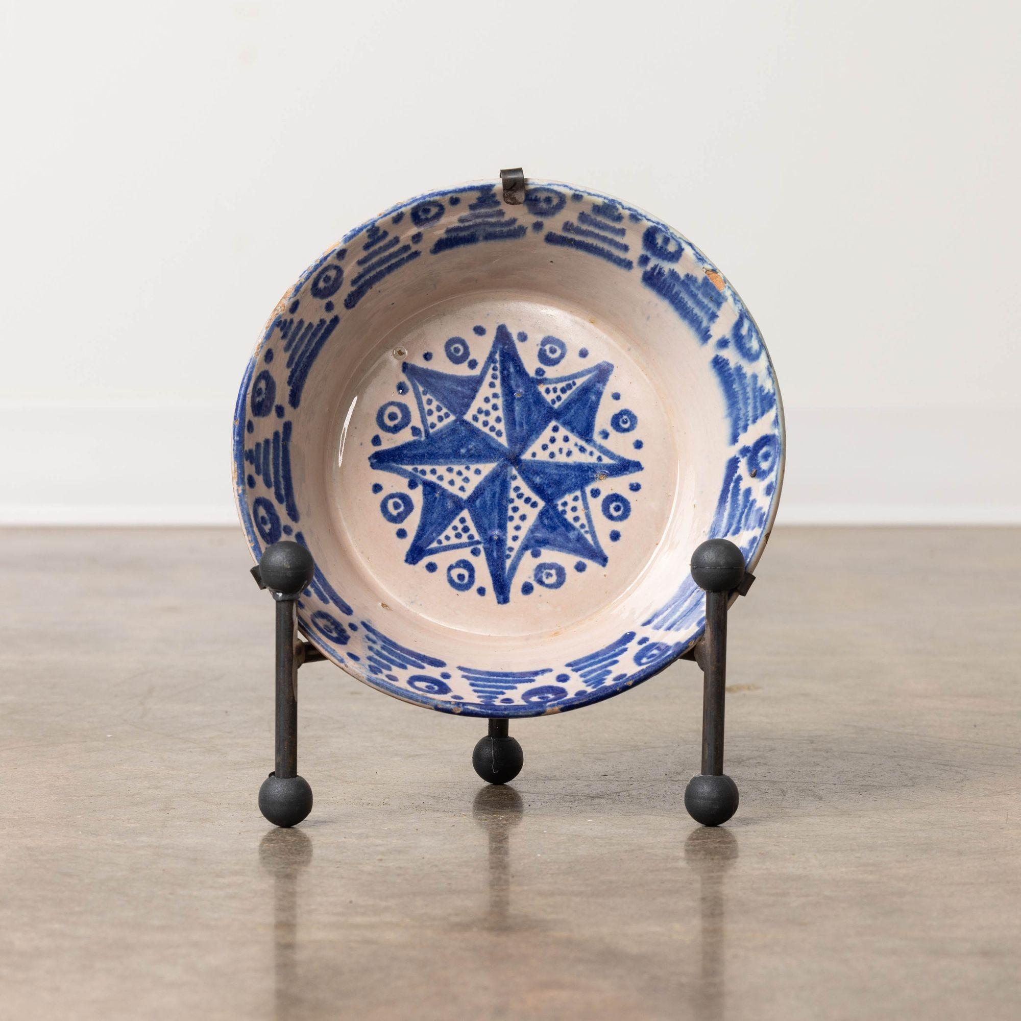 Schale aus Steingut aus Granada, Spanien, 19. Jh., blau bemalt, milchweiße Glasur. Diese tiefe Schale zeichnet sich durch ein handgemaltes Sternmotiv auf dem Schalenboden und dekorative Seiten aus. Verkauft mit einem handgeschmiedeten Eisenständer