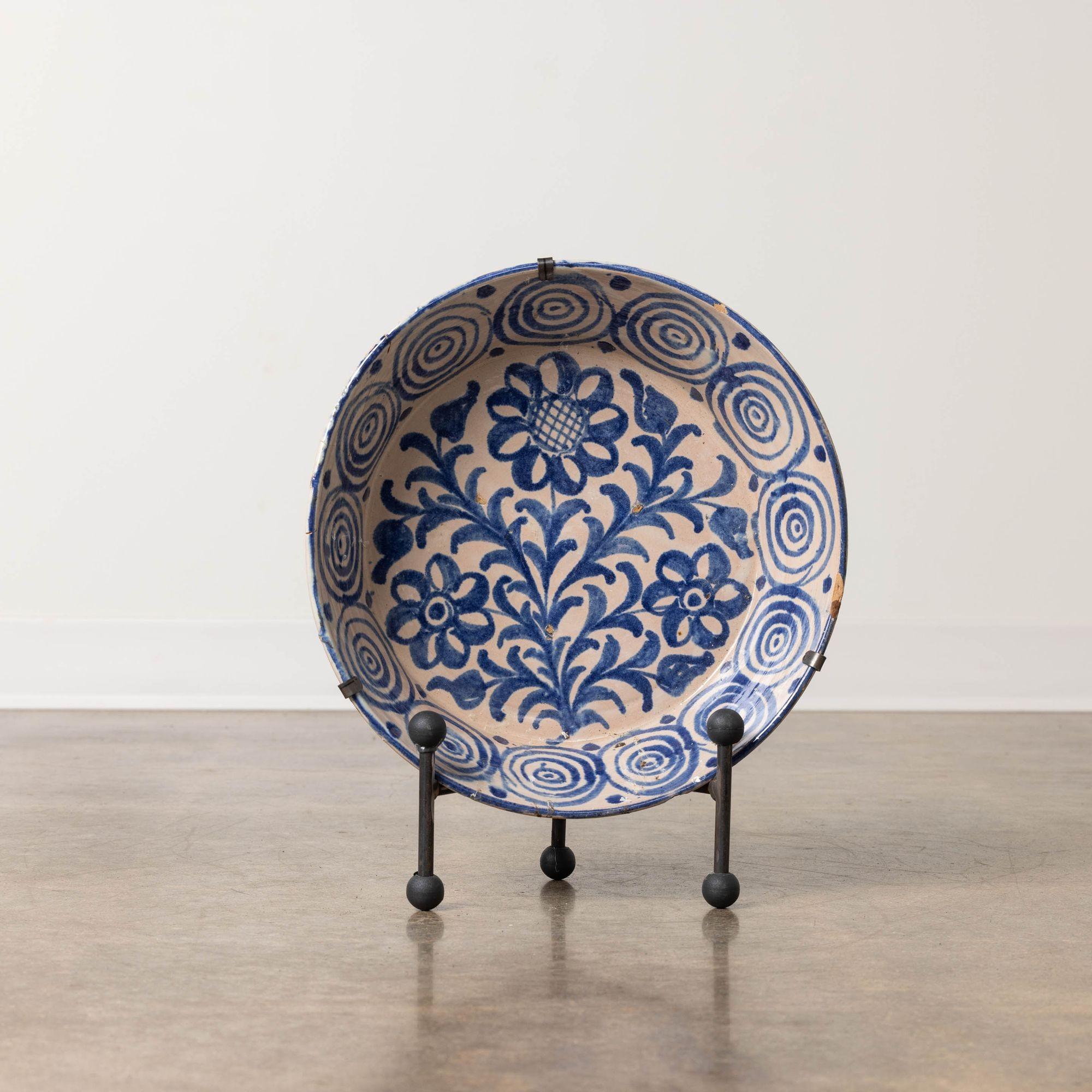 19th c. earthenware bowl from Granada, Spain painted in blue over a milk-white glaze. This deep bowl features a hand-painted floral and leaf motif on the bottom of the bowl with decorative sides. Sold with both a hand-forged iron stand and