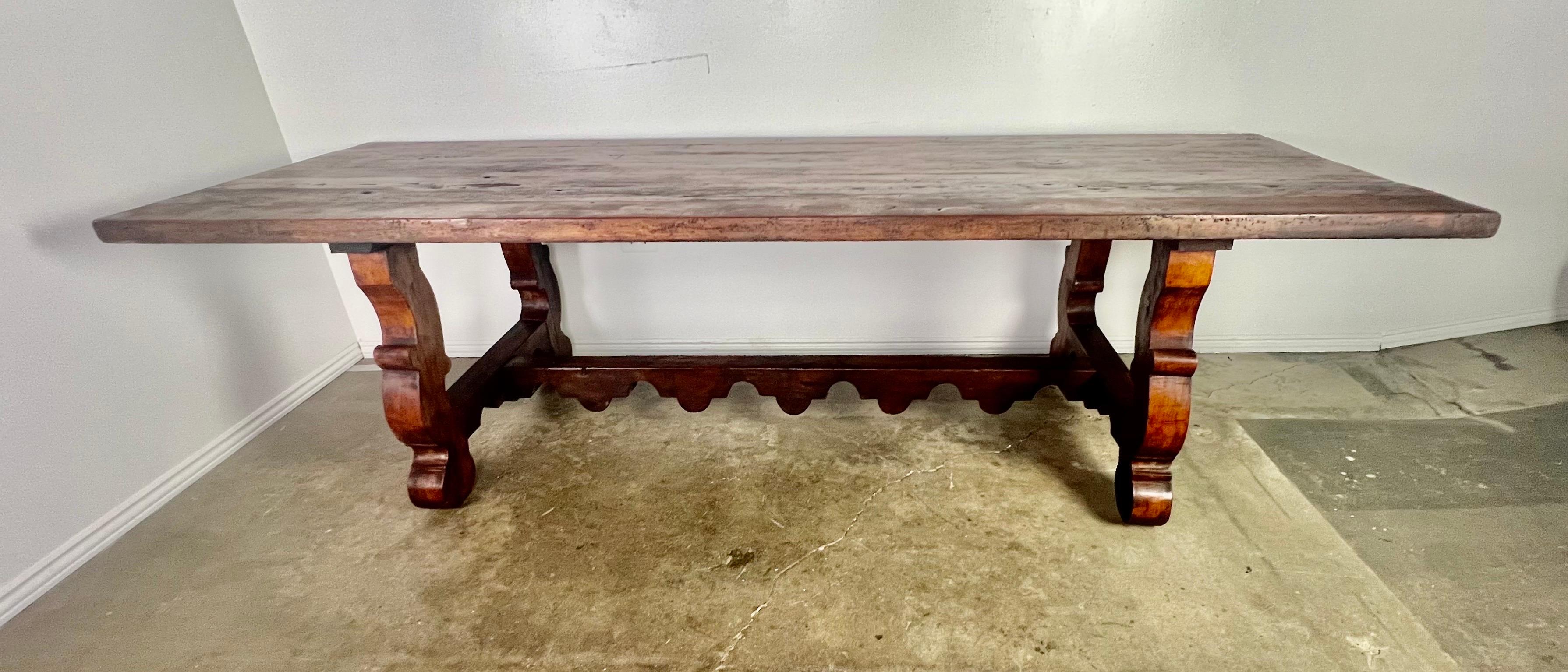 19th century Spanish pine refractory table. The table stands on two pedestal bases connected by a scalloped stretcher. Wear is consistent with age and use of the table.