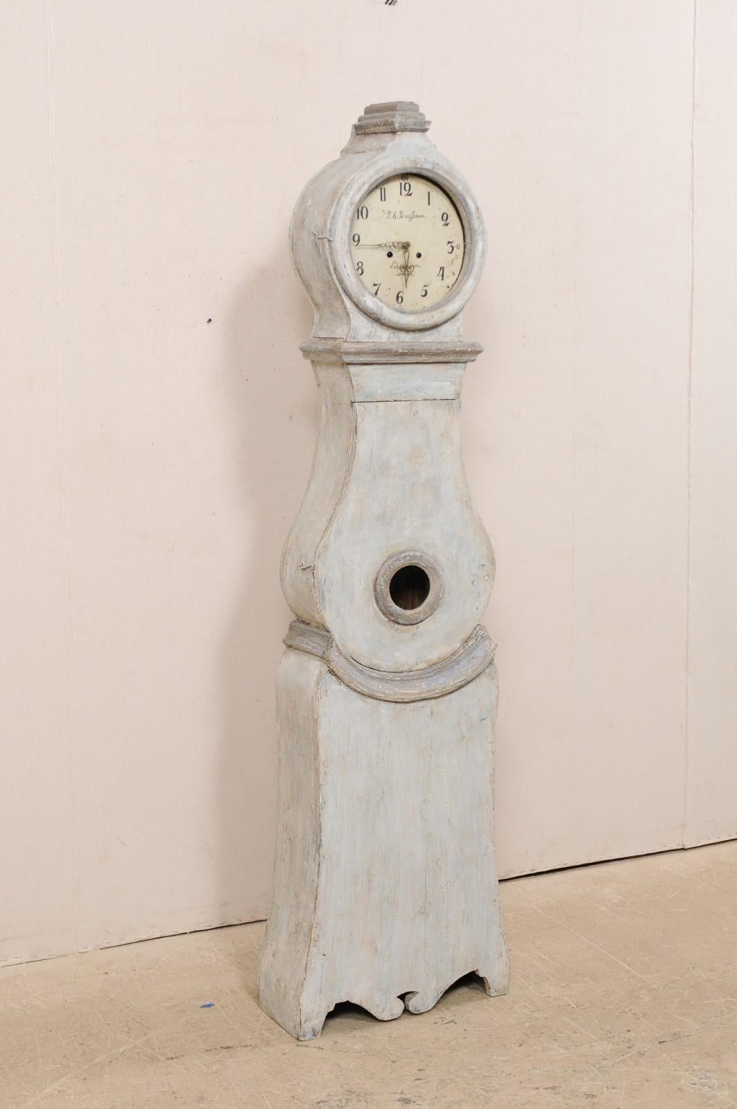 A Swedish Fryksdahl carved and painted wood floor clock from the 19th century. This antique Swedish Fryksdahl clock features a carved crown which tilts slightly forward, adorn with a central volute at arched crest. The rounded head is gives way to a