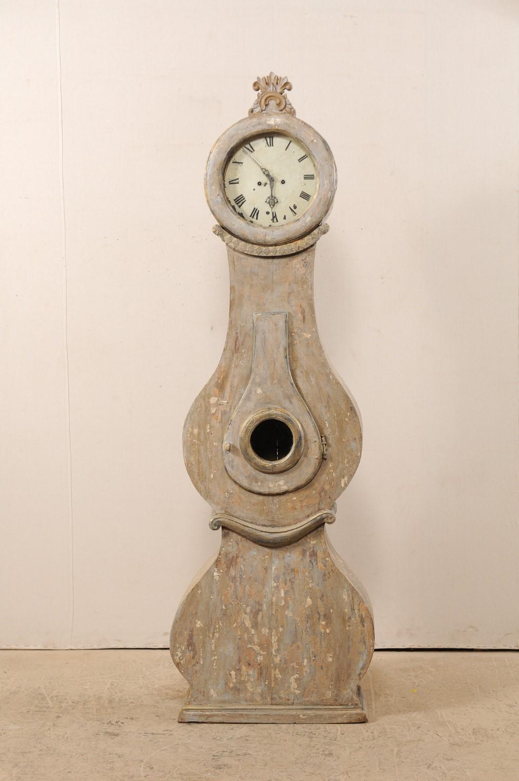 A 19th century Swedish Fryksdahl clock with shapely body and carved crown. This antique Fryksdahl clock from Sweden has a raised crest, carved in c-scroll with splaying foliage rising out of the top, a rounded head, and diamond and floral carved