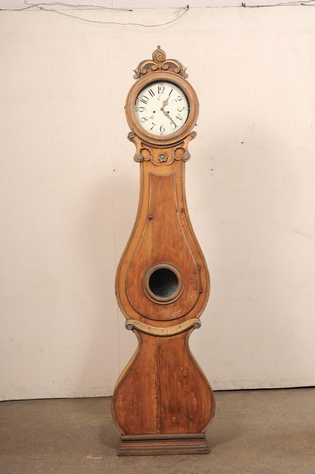 A Swedish Fryksdahl floor clock from the 19th century. This antique Fryksdahl clock from Sweden, circa 1820's, has a beautifully carved crest/bonnet top over its rounded head, with petite flowers and volute accents embellishing the neck. The tear