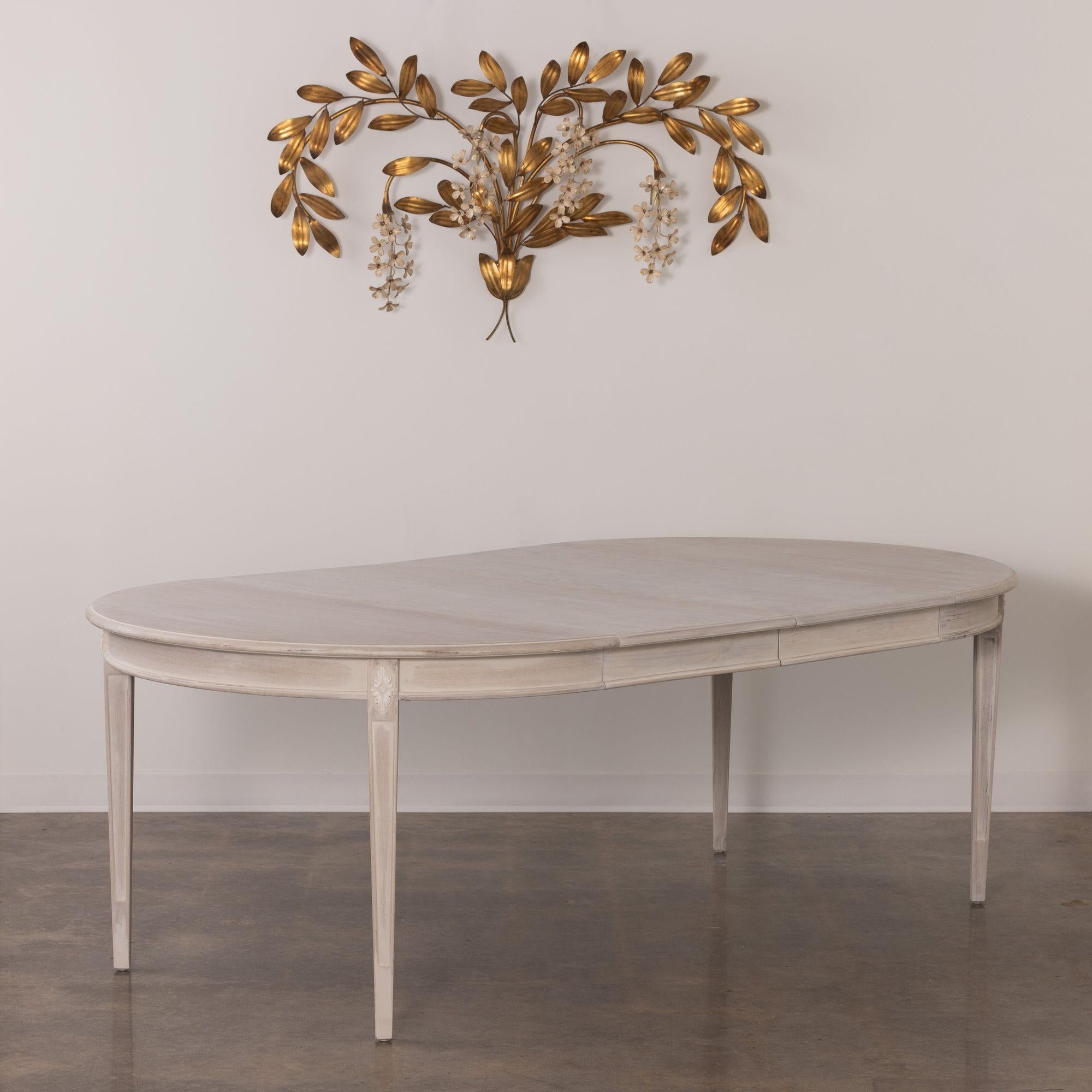 A beautiful, bleached and glazed Swedish Gustavian style oval dining table with three leaves. There is a carved rosette above each square and tapered leg. Two leaves are made of maple and each are 19.38 inches wide.  And, one leaf included is made
