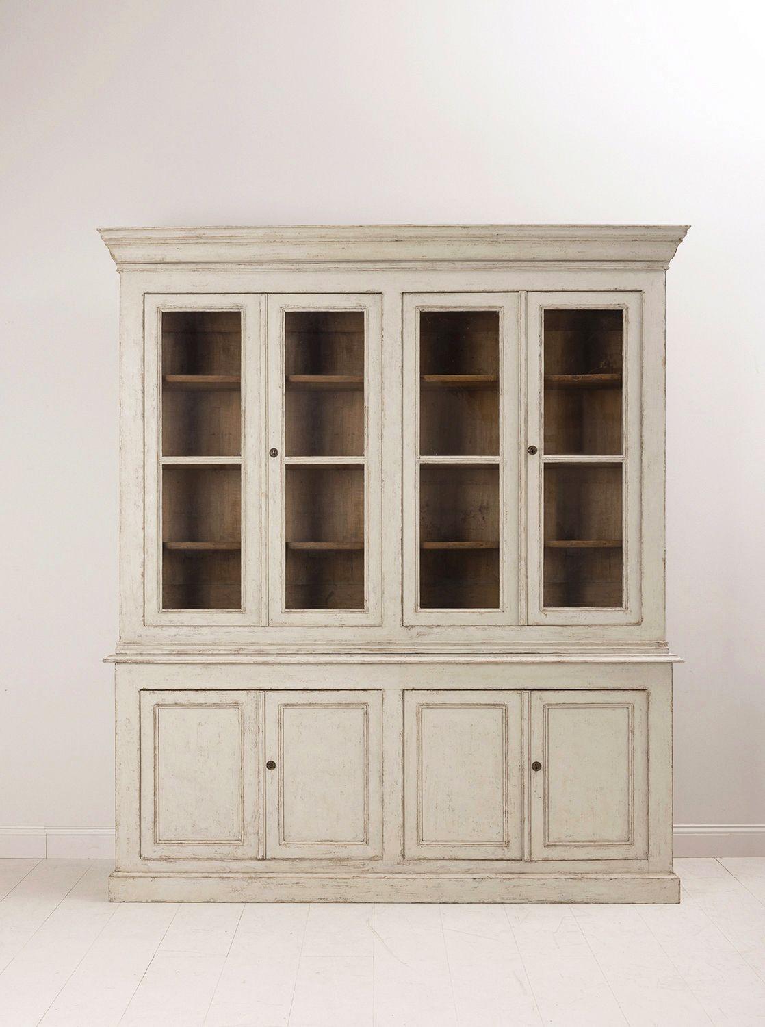A Swedish Gustavian four-door painted vitrine cabinet from the 19th century. This classically designed piece is made in two parts. The upper section features three fixed shelves behind original glass doors. Below there are four doors that open to