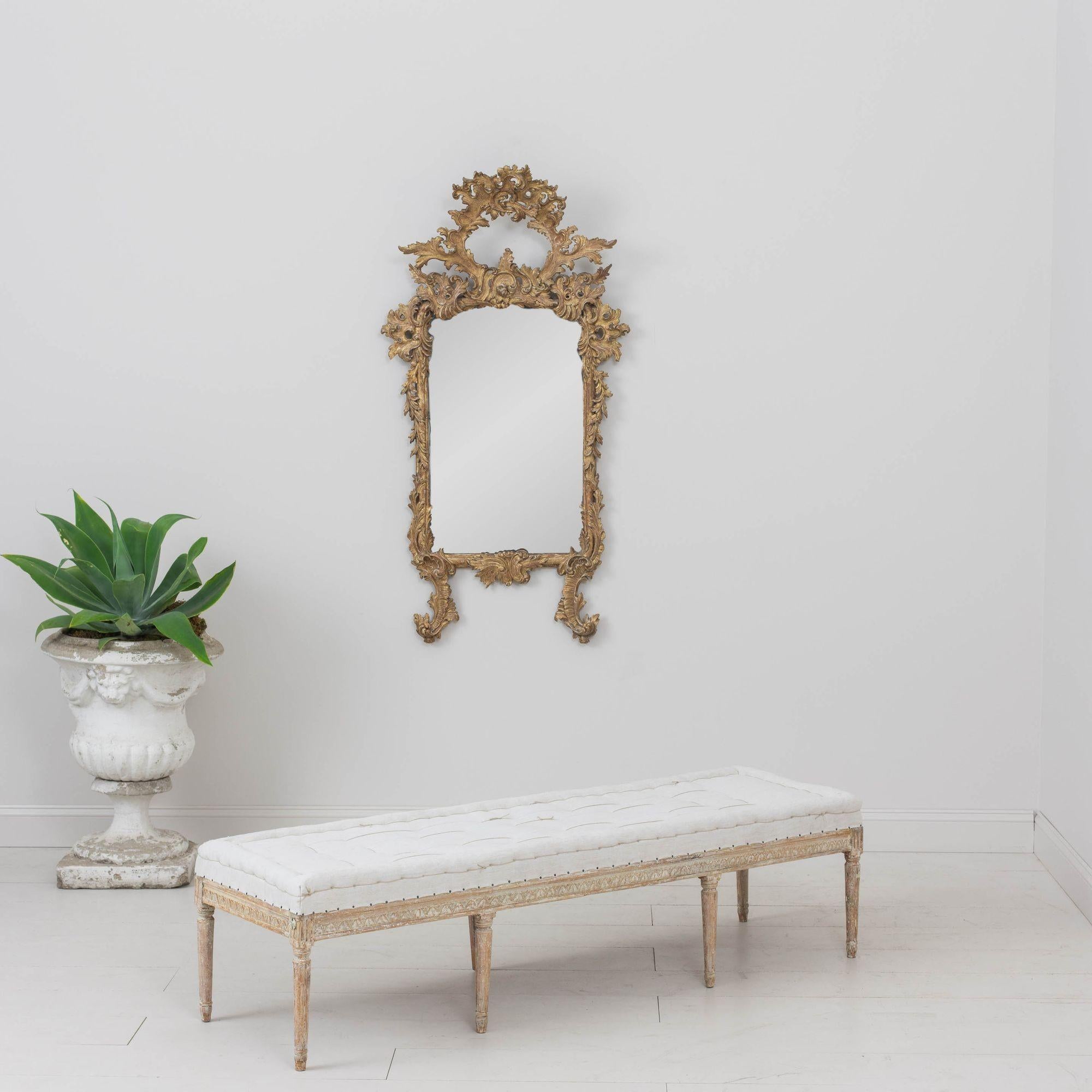 This is a richly carved 19th century Swedish Gustavian period bench, newly upholstered with a hand-stitched, tufted linen seat with nail head trim. The paint has been hand-scraped to reveal the original chalky white paint surface with areas were the