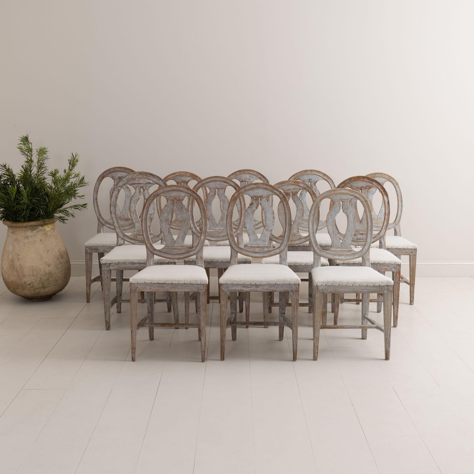 A collection of twelve similar 'Swedish Model' chairs from the Gustavian period, hand-scraped to the original paint surface and newly upholstered in linen. These beautiful, provincial chairs have oval pierced backs and fluted legs with cross