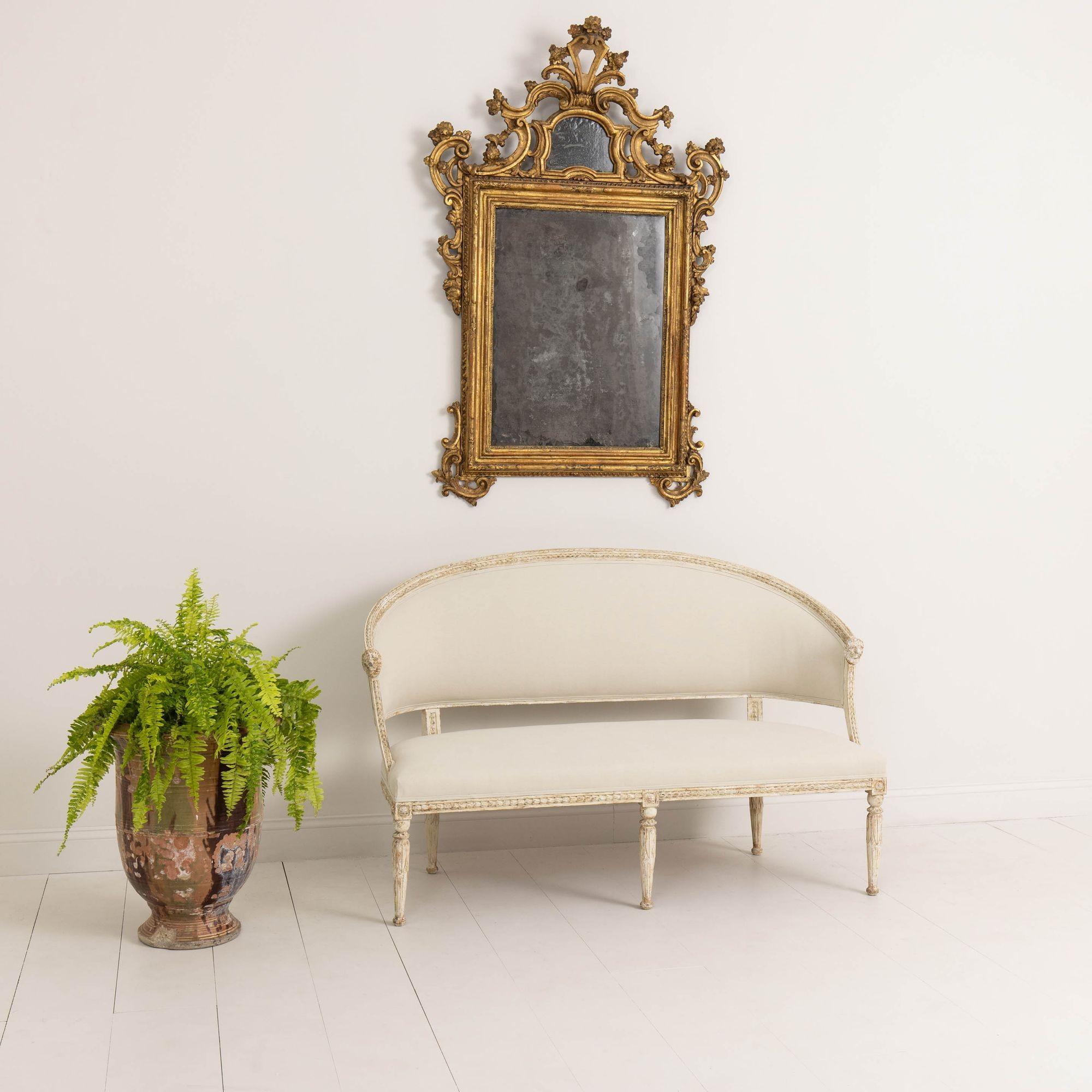 A beautiful 19th century Swedish barrel back sofa settee in the Gustavian style, newly upholstered in linen, circa 1890. Hand scraped to reveal the original paint. The frame features carved bell flowers, lion heads on the arms, lotus flowers on the