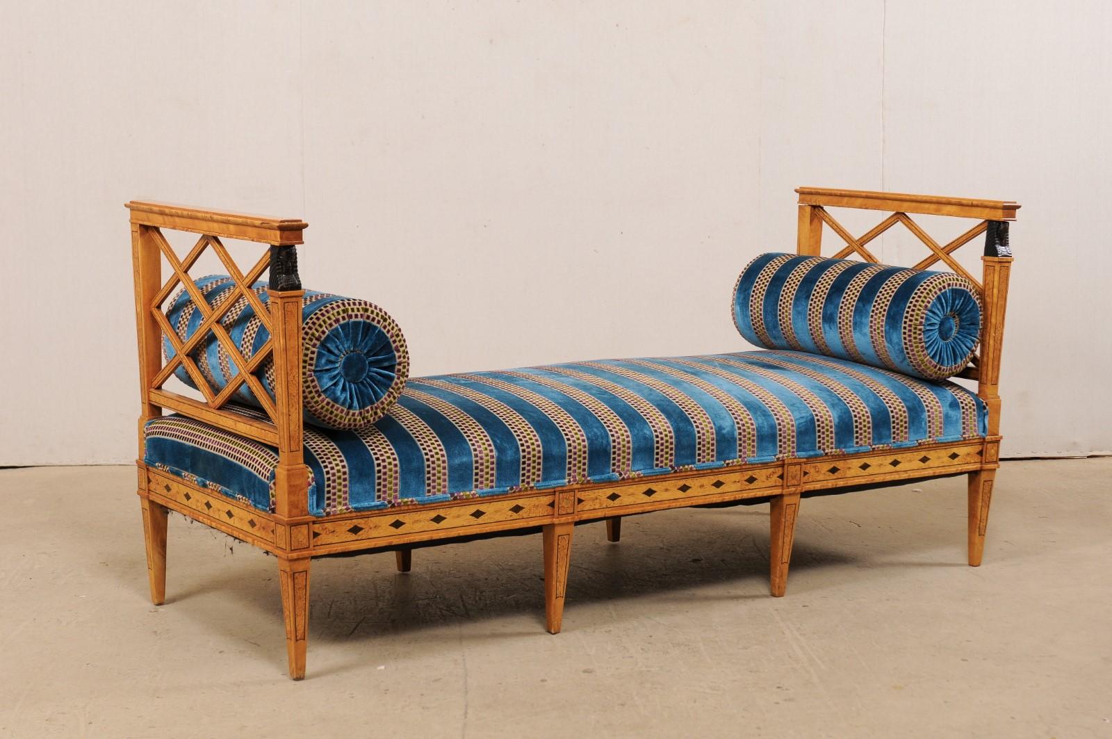 A Swedish neoclassical style bench from the 19th century with upholstered seat. This antique bench from Sweden features a neoclassical design with Egyptian Revival carved arm posts, and is made of birch wood with burl inlay and ebonized wood