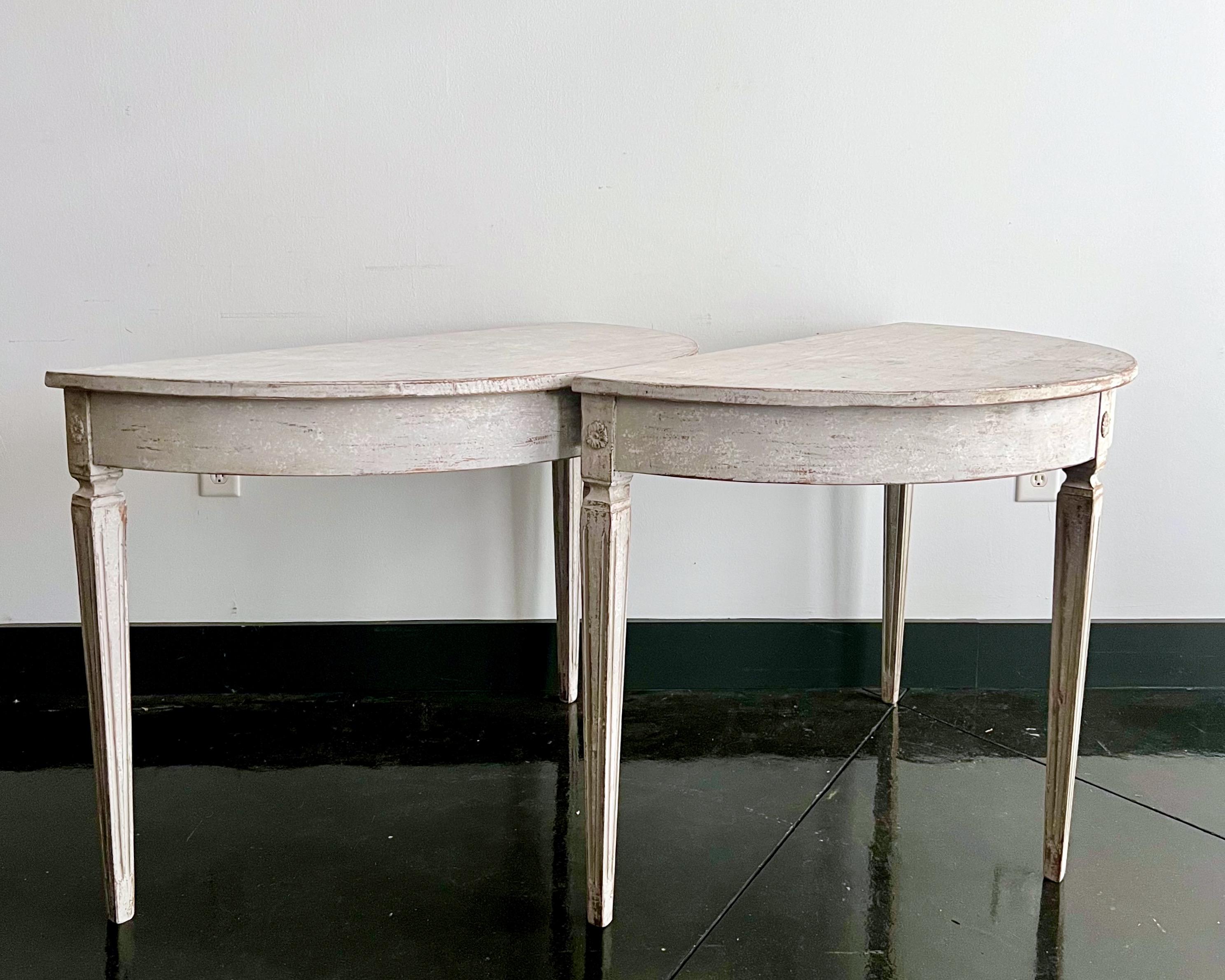 Pair of Swedish Neoclassical period demilune console tables with wide rounded apron and florets on the corner blocks. Elegant tapered and fluted legs.
Many layers of newer paint scraped to its most original finish.
Stockholm, Sweden, circa 1820.