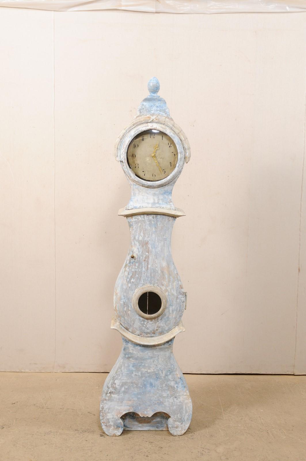 A Swedish long-case carved and painted wood floor clock from the 19th century, with new quartz movement. This antique floor clock from Sweden, has an exaggerated bonnet topped with egg-shaped finial. The clock has a distinctly curvy rain-drop shaped