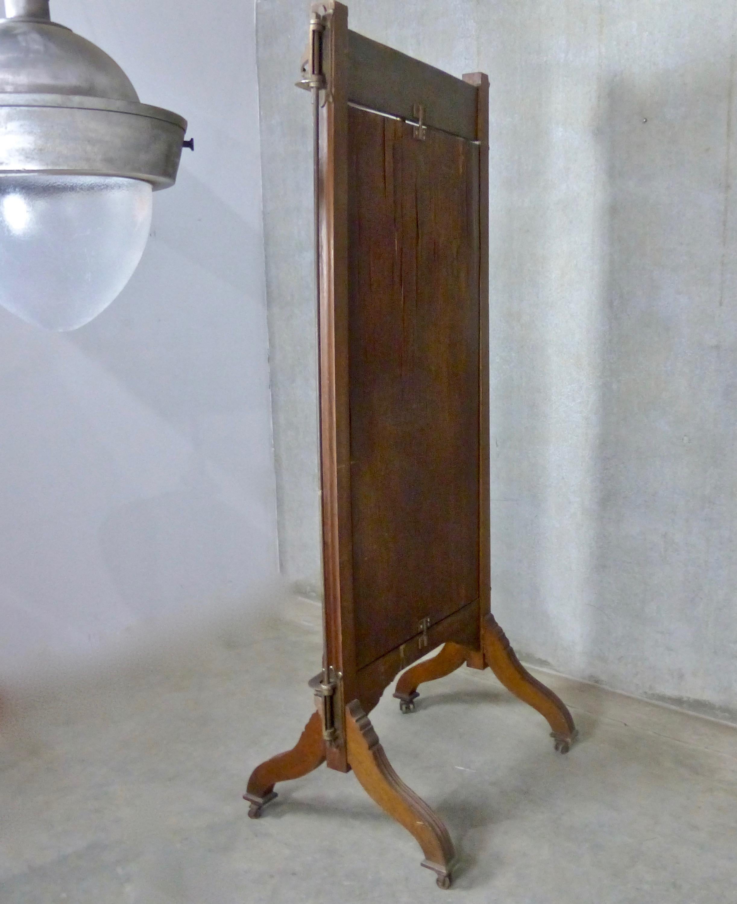 A circa 1890 tri-fold mahogany vanity mirror on wheels. Made by John Willard, New York City, the freestanding mirror features nicely carved details in the wood plus cast iron articulating arms. Folds into a compact, single panel to save space when