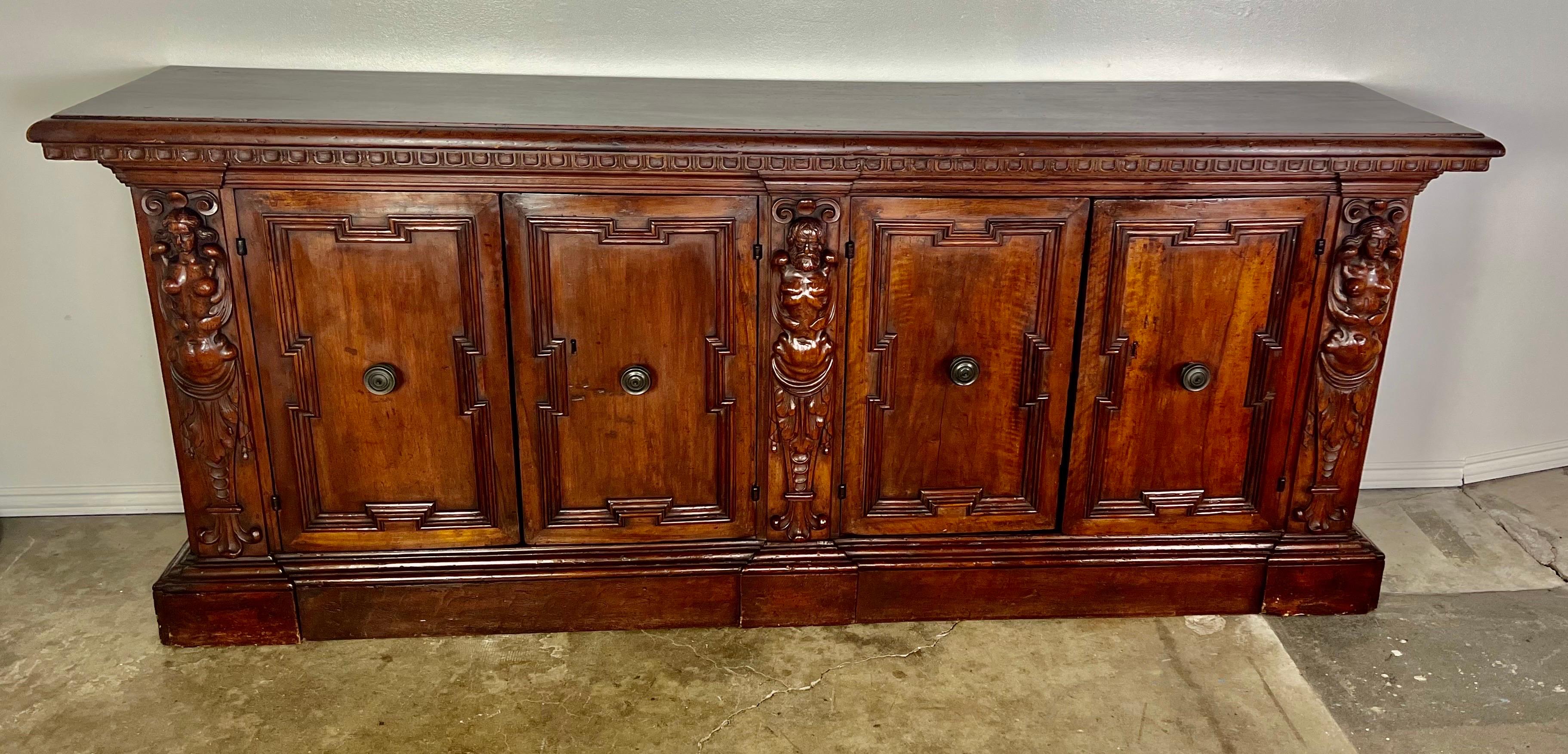 A 19th-century walnut Italian credenza with intricate carving is a stunning piece, showcasing the craftsmanship of that era.  The detailed figural carvings that flank the two pairs of doors, add aesthetic appeal and historical value to the credenza.