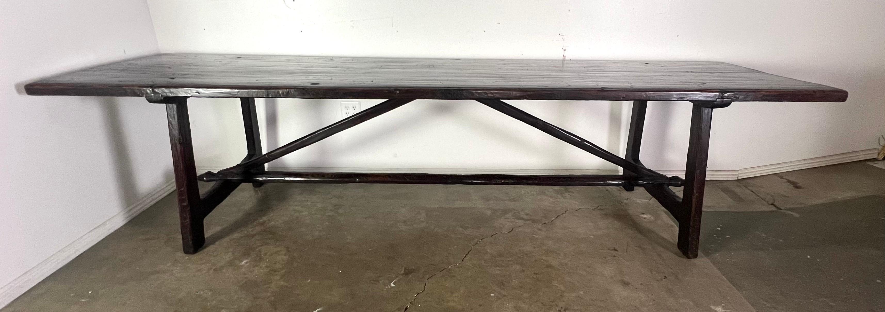 19th century Italian primitive style dining table.  It has a rectangular top and a dark, rich patina.  The legs and supports are also wooden and have a robust construction, with diagonal supports for additional stability.

