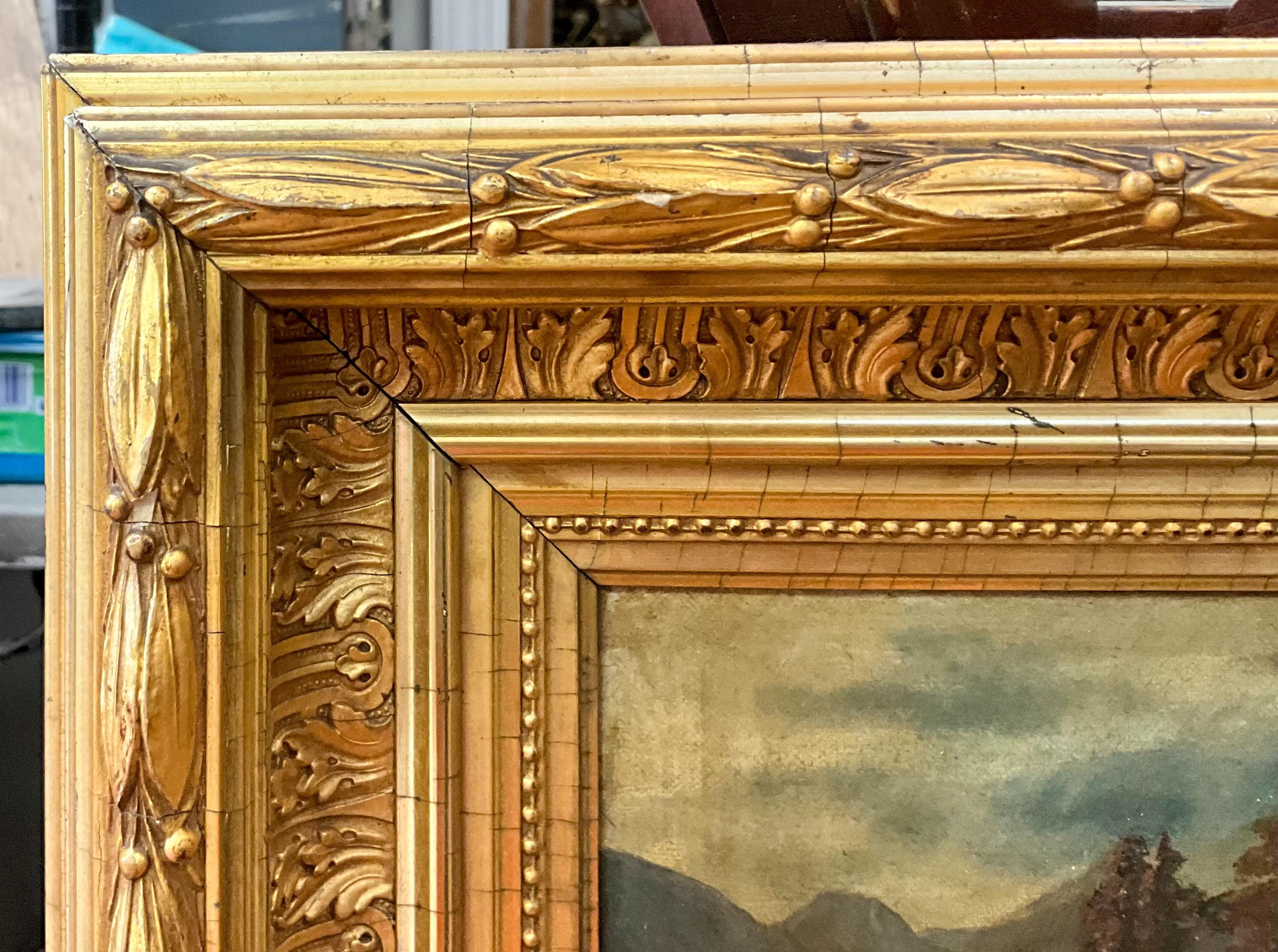 This is a late 19th century American oil on canvas depicting a scenic river scene with and old mill and pine trees. There is no visible signature. The water gilt frame is lovely with its carved acanthus and bellflowers. It has age appropriate wear. 