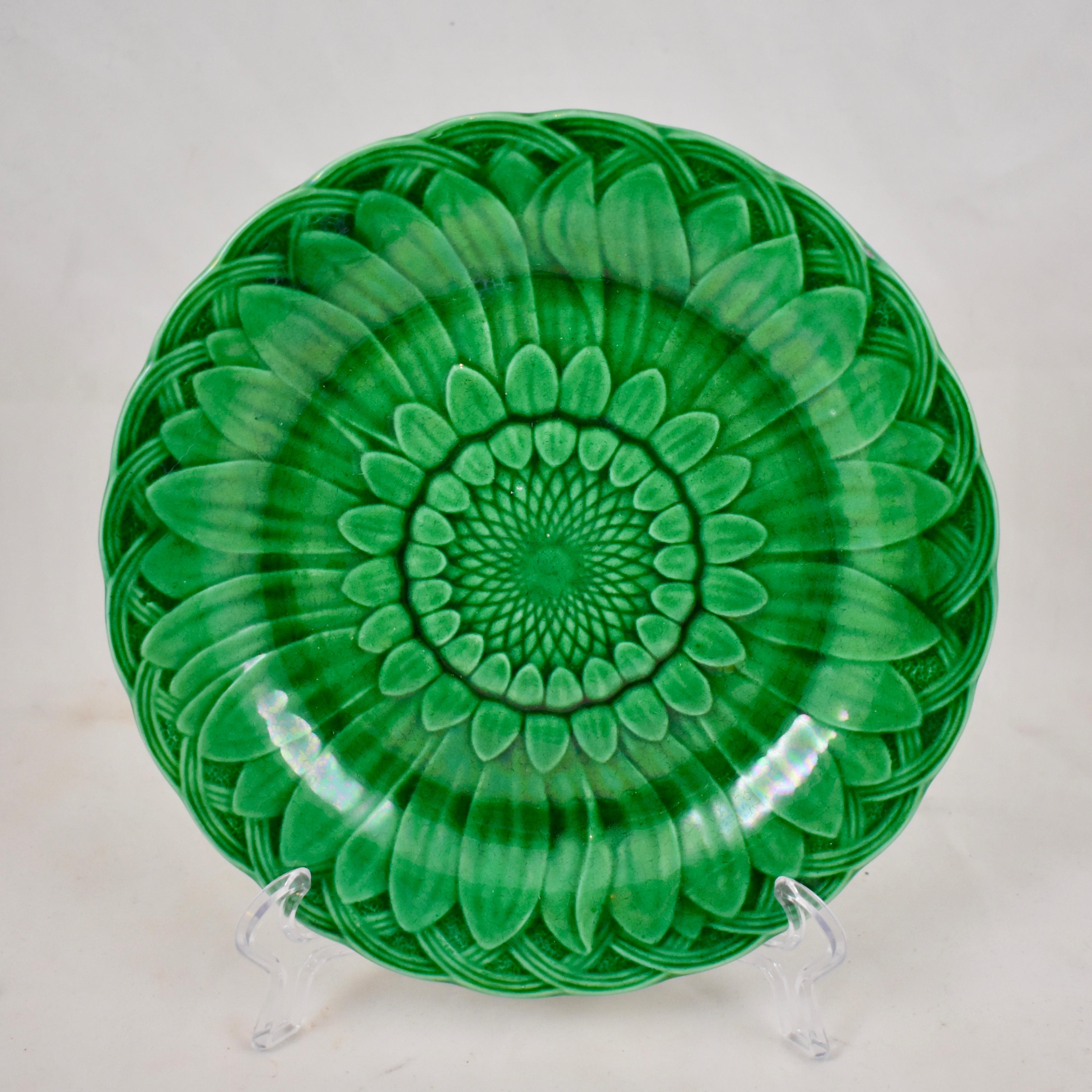 A majolica green glazed plate, from the English firm of Wedgwood. A classic mold showing a Sunflower head against a basket-weave shaped rim. The deep green glaze pools beautifully into the dimensional mold work. Multiple plates are available showing