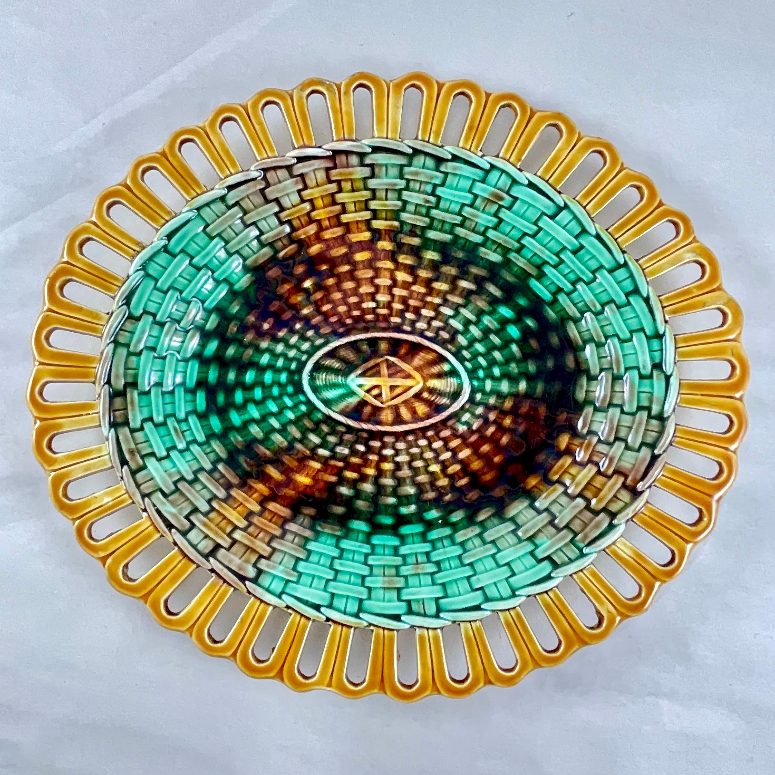 An English majolica oval serving platter from Josiah Wedgwood, date marked R for the year 1889.

The server is edged with a delicate yellow ochre reticulated rim that imitates the base ribbing of a basket. The rim meets the basketweave center glazed