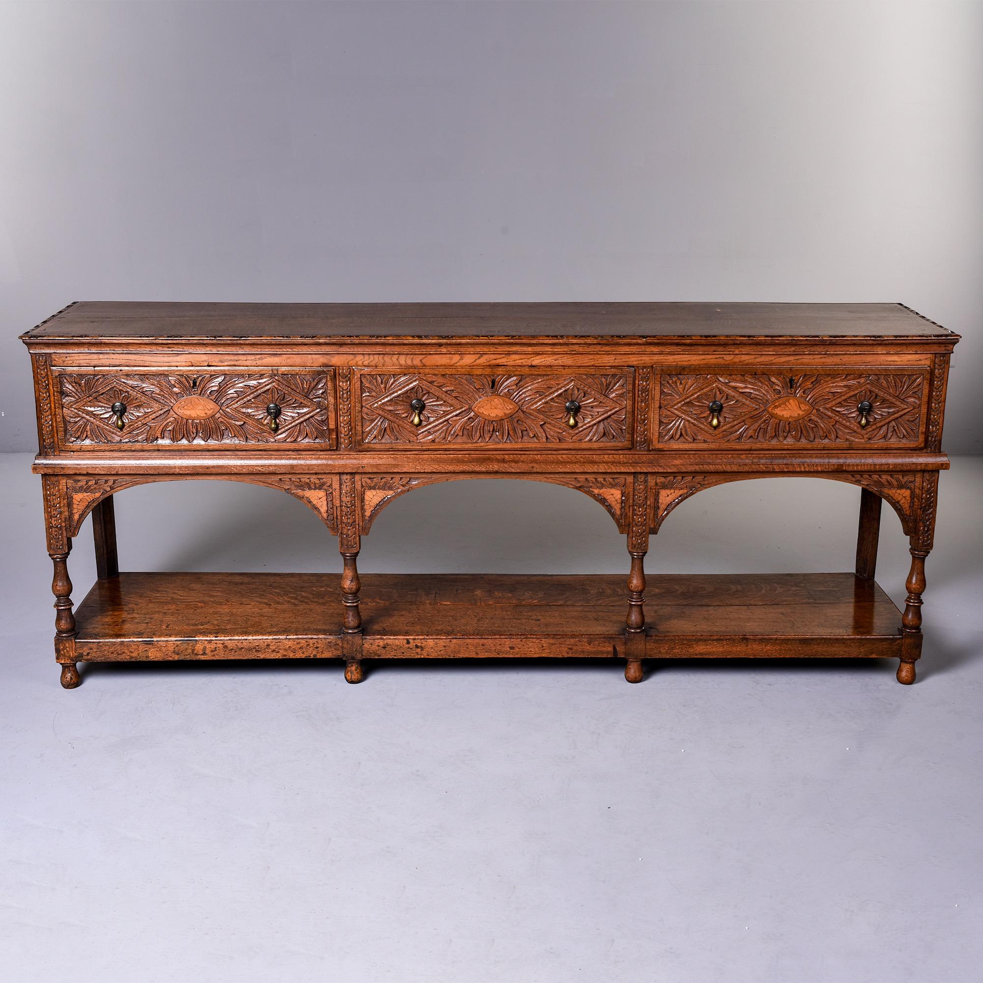Circa 1880s Welsh oak dresser base with detailed carving makes a great console. Three functional drawers with dovetail construction, botanical / leaf form chip carved fronts with a fancy whelk type shell rendered in contrasting inlay at the center