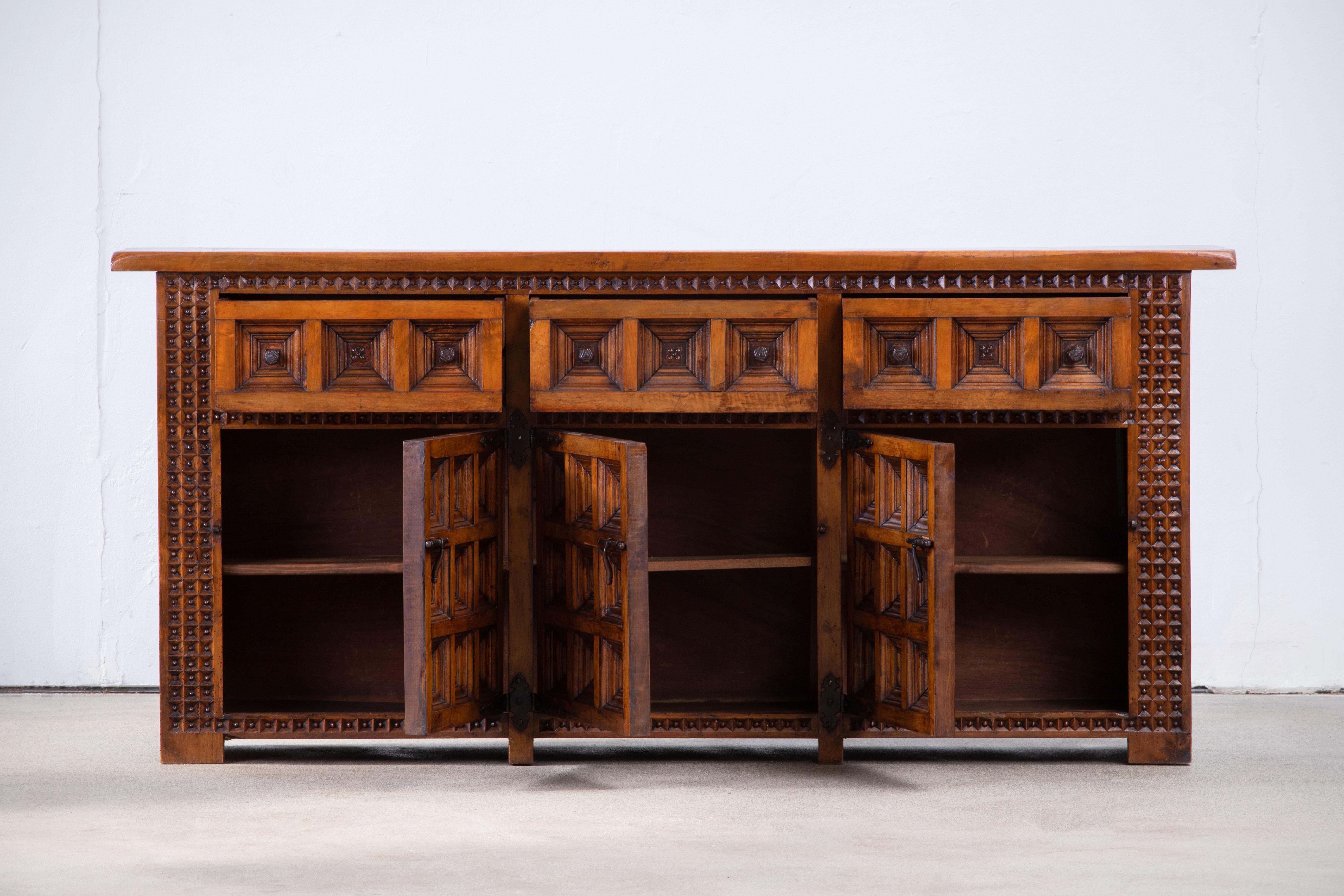 From Northern Spain, constructed of solid walnut, the rectangular top with molded edge a top a conforming case housing two drawers over two doors, the doors paneled with solid walnut, raised on a plinth base.
 