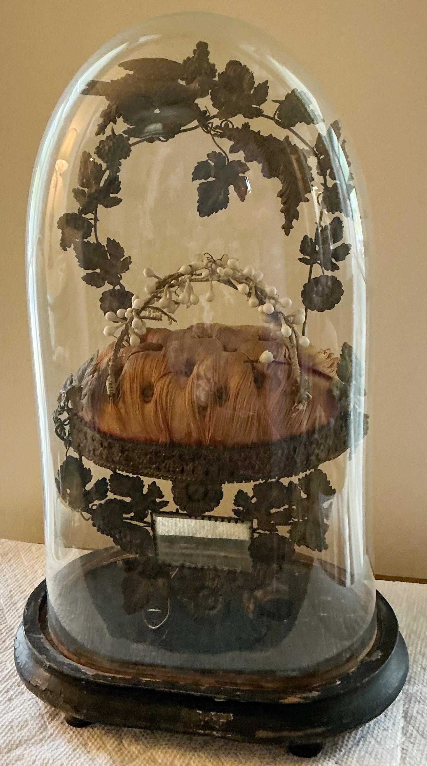 This is an amazing example of Victorian culture. It is a bride’s crown displayed on a tufted silk pillow with brass birds circling the piece. There is a small mirror at the base of the display. The glass cloche is original and fits nicely in the