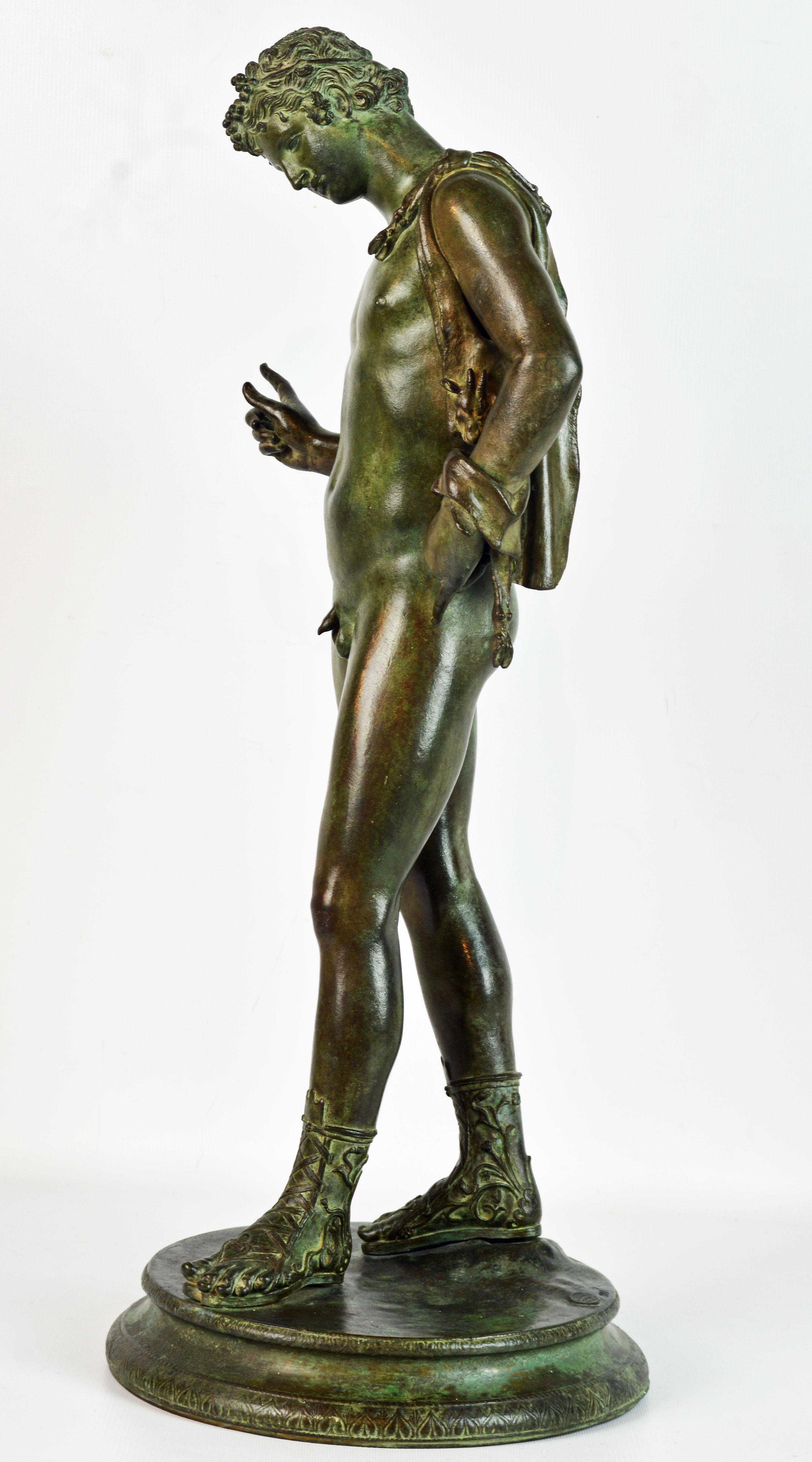 Une grande statue en bronze magnifiquement patiné de Narcisse portant un sac à vin en peau de chèvre sur son épaule reposant sur une base ronde finement décorée. La base porte la marque de fonderie de Vicenzo Gemito et est numérotée. Cette figure
