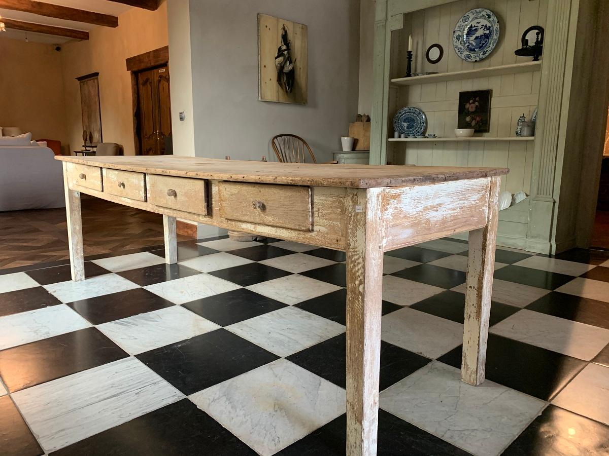 A early 19th century French oak and poplar farmhousetable. The supports with original white paint remains and the top in naturally bleached poplar. 4 Drawers on one side and panneling on the other. The top slightly bend.