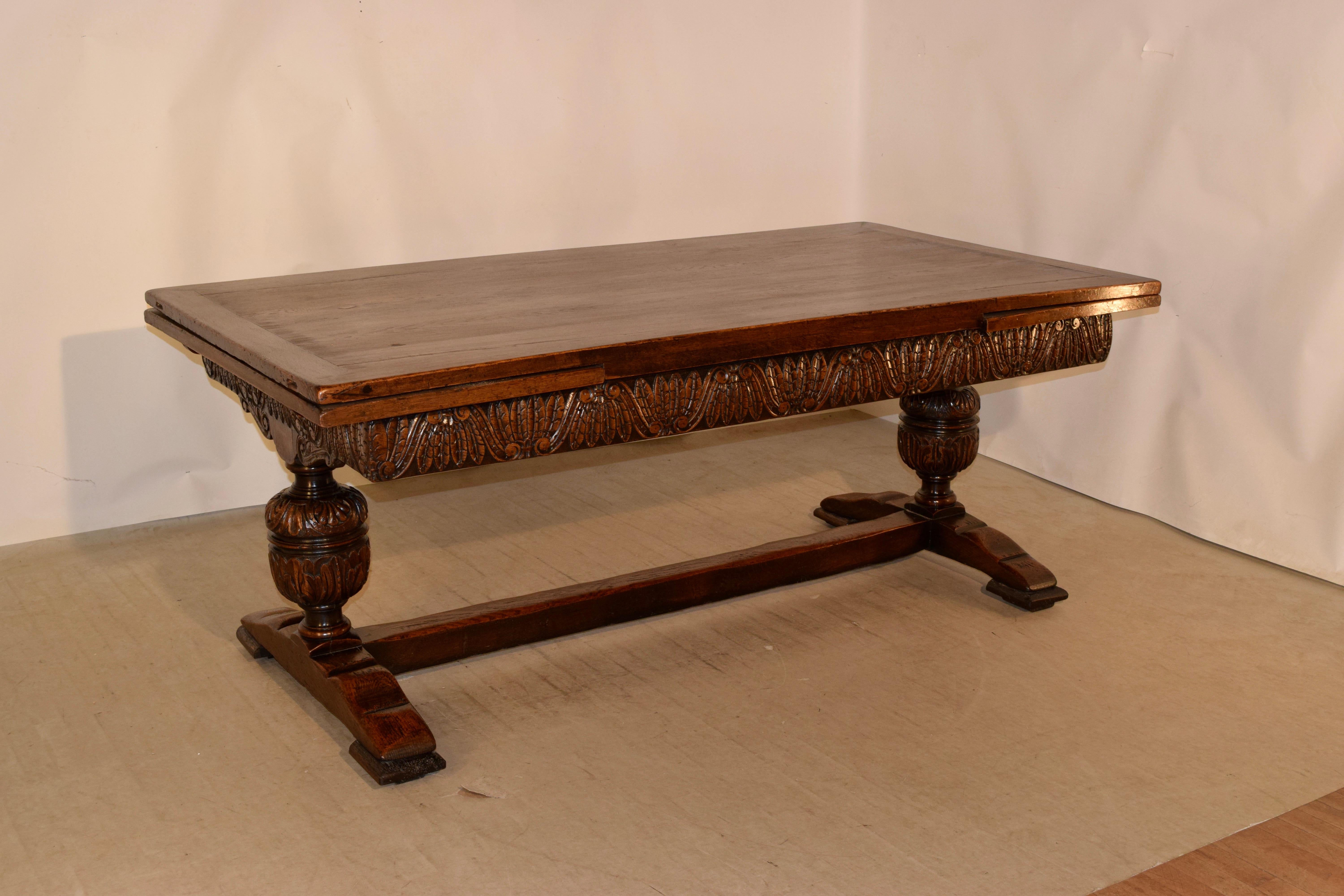 19th century massive oak table from England with draw leaves. The top is banded and has two leaves which draw out for an extended length of 120 inches. The top is supported on a trestle base, which has a wonderfully hand carved decorated apron and