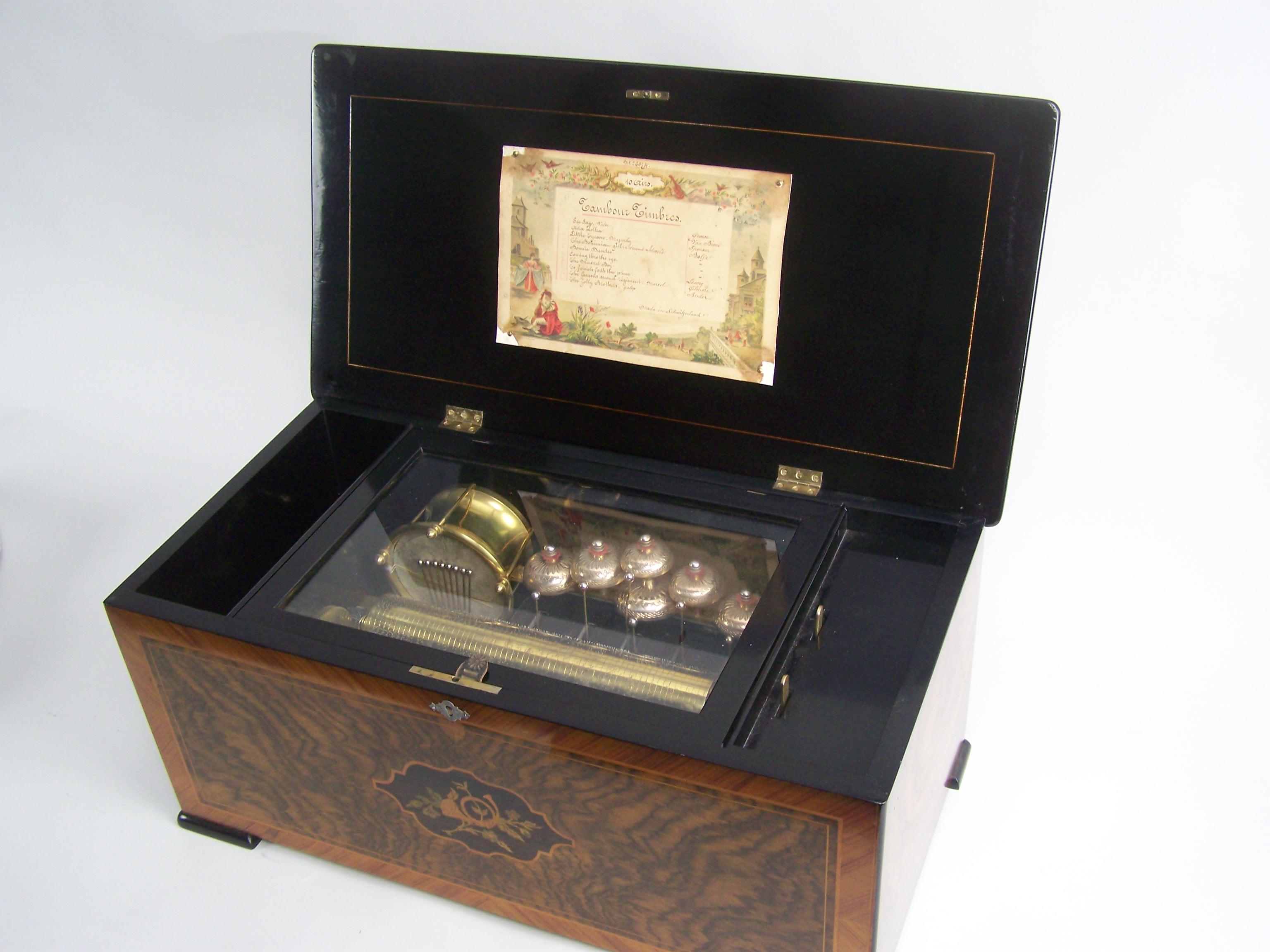 Exposed drum and bells music box.
Playing 10 tunes as indicated on the original tunesheet. 
The inlay to the front and lid is polished, the inside iof the case is black polished. The mechanism has a 28cm cylinder and play very vivid and joyfull
