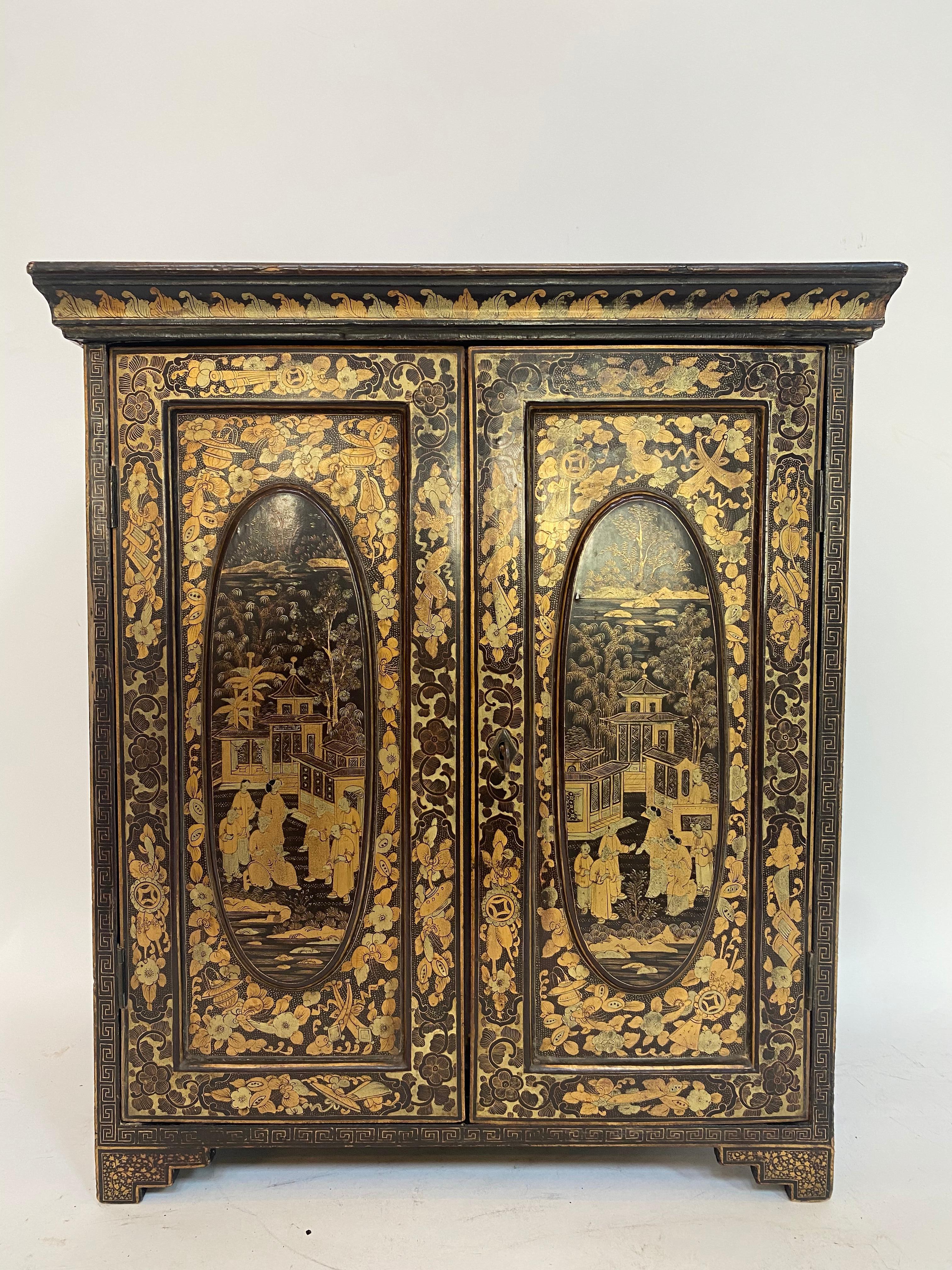 19th century antique hand painted Chinese lacquer jewelry cabinet with a pair of raised panel doors opening to five drawers with turned ivory handles, decorated throughout gilt with scenes with figures, pavilions trees and flowers in a black ground,