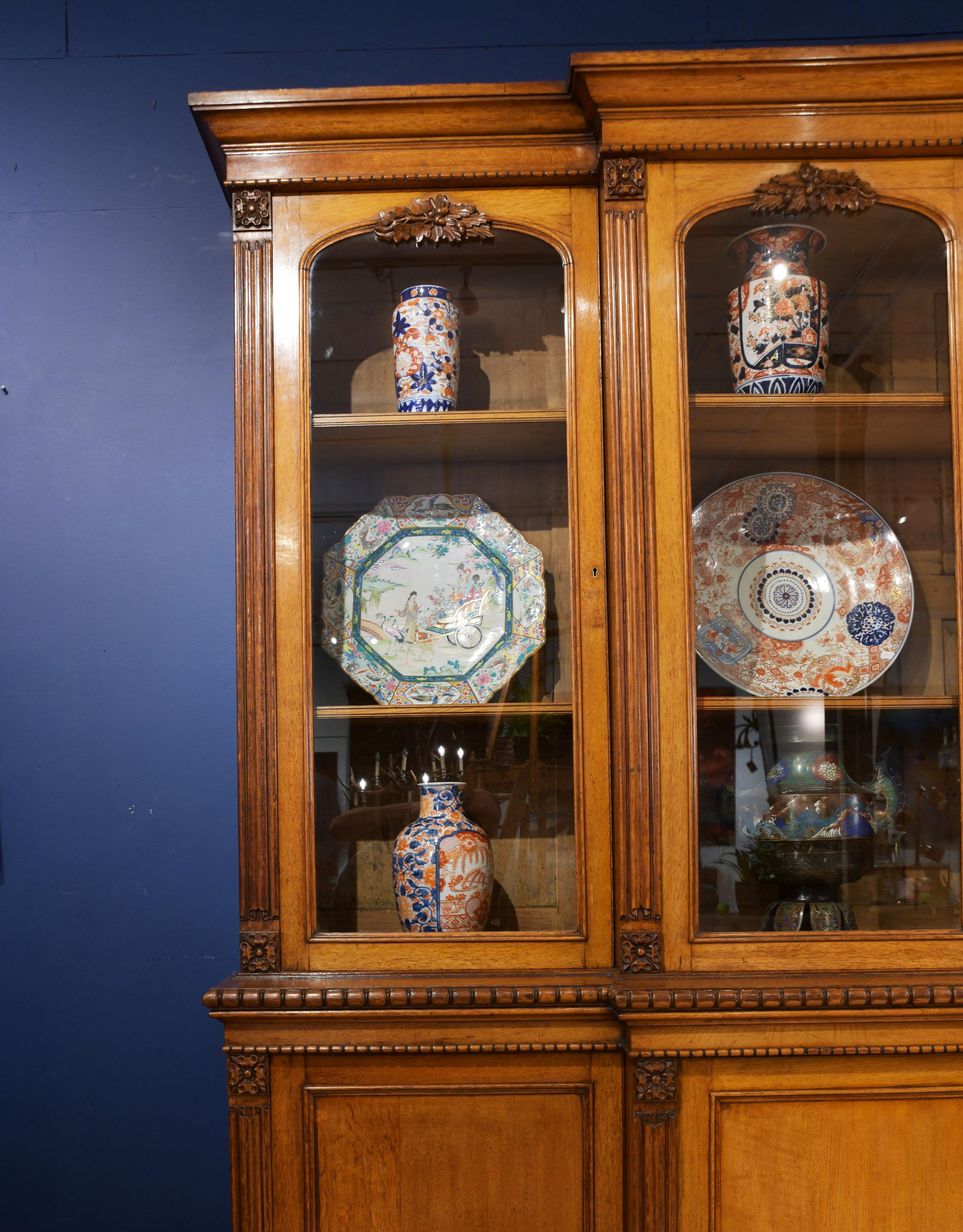 This magnificent and substantially sized English oak bookcase features linen fold carving and acorn leaf detailing above each glass paneled door. A Lobe molded edge divides the top and bottom section, both with adjustable shelves. The bookcase