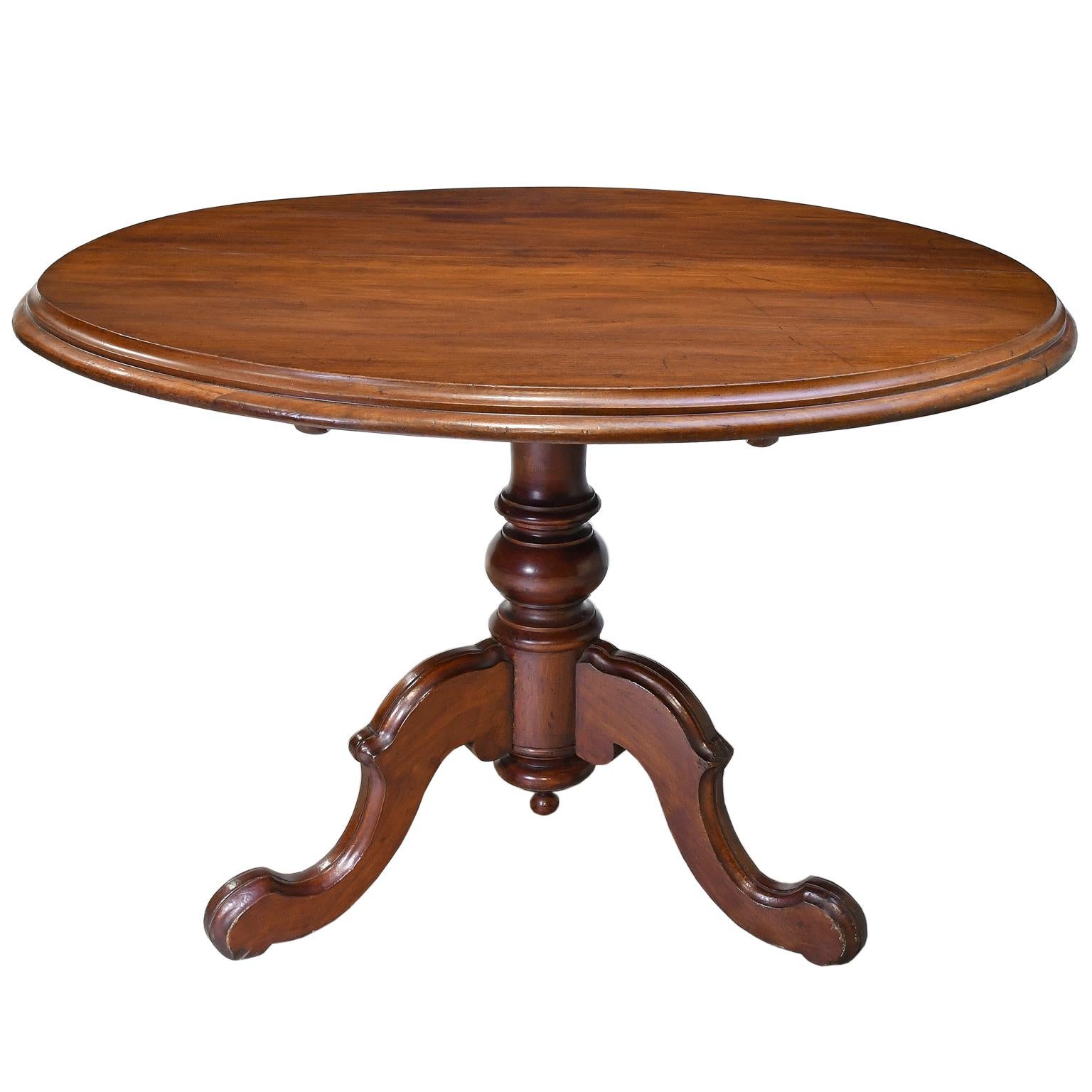 A lovely round dining table in walnut on baluster-turned column over carved tripod base, with tilt-top mechanism. A very sturdy and mechanically-sound table with a relaxed finish, showcasing the patina acquired over time. Original hardware. England,