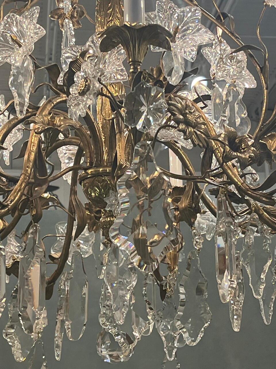 Experience the opulence of the 19th century with this exquisite Rococo-style crystal chandelier. Adorned with intricate floral motifs and gilded accents, its eight bulbs cast a soft, romantic glow, transforming any space into a grand ballroom or an