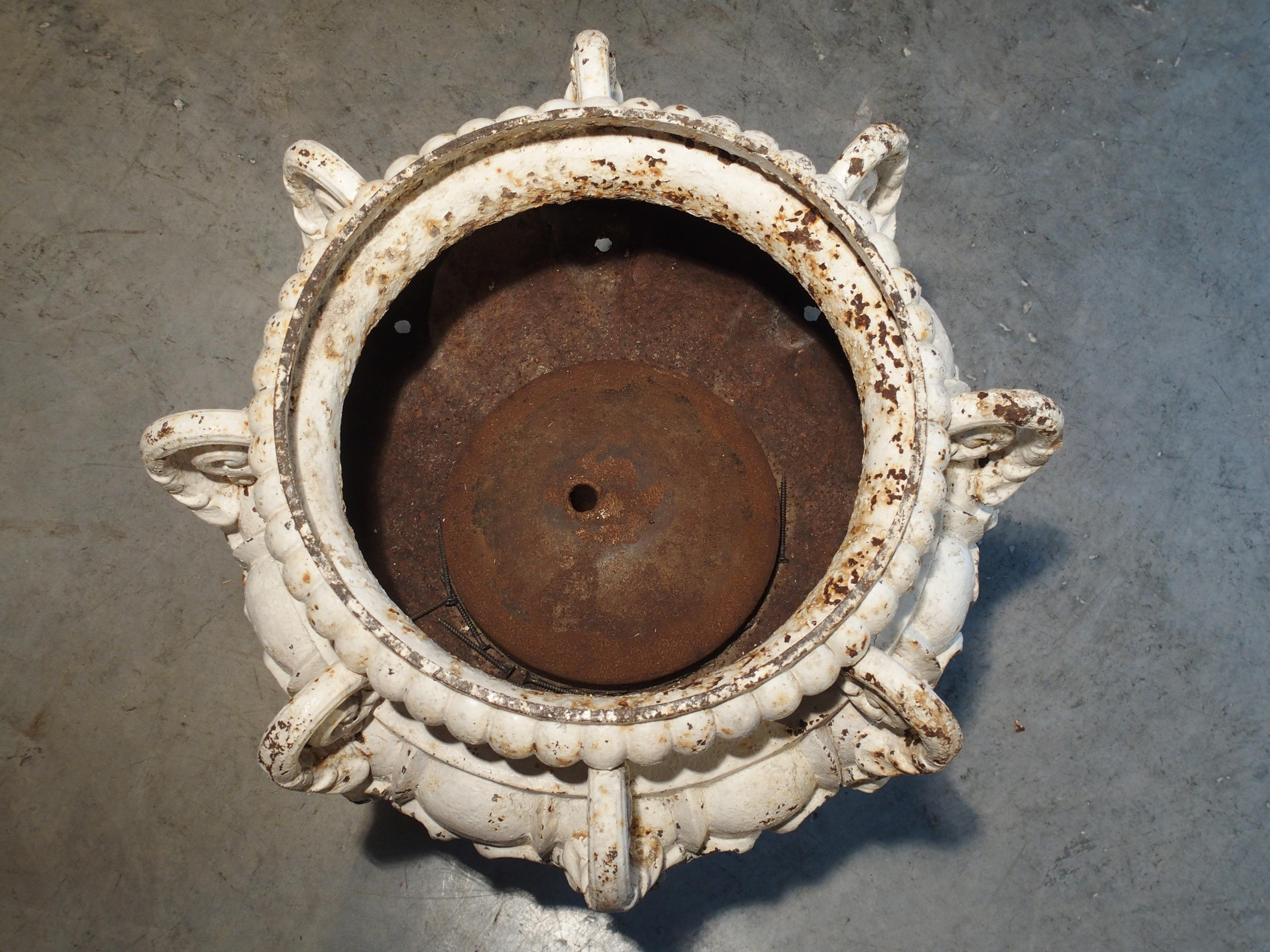 Dieses prächtige Brunnenelement aus lackiertem Gusseisen hat 8 Ausgüsse:: die aus den Mündungen der Maskaronen am Boden der Urne kommen. Sie stammt aus dem 19. Jahrhundert und ihr oberer Rand ist rundherum mit Zacken versehen. Über den Köpfen der