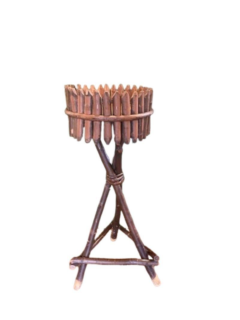 Antique Adirondack Twig Fern Stand, Late 19th Century, a handcrafted pedestal stand made from black cherry branches, having a round pine board top with an applied stockade gallery of whittled and halved branch posts, raised on a crossed tripod of