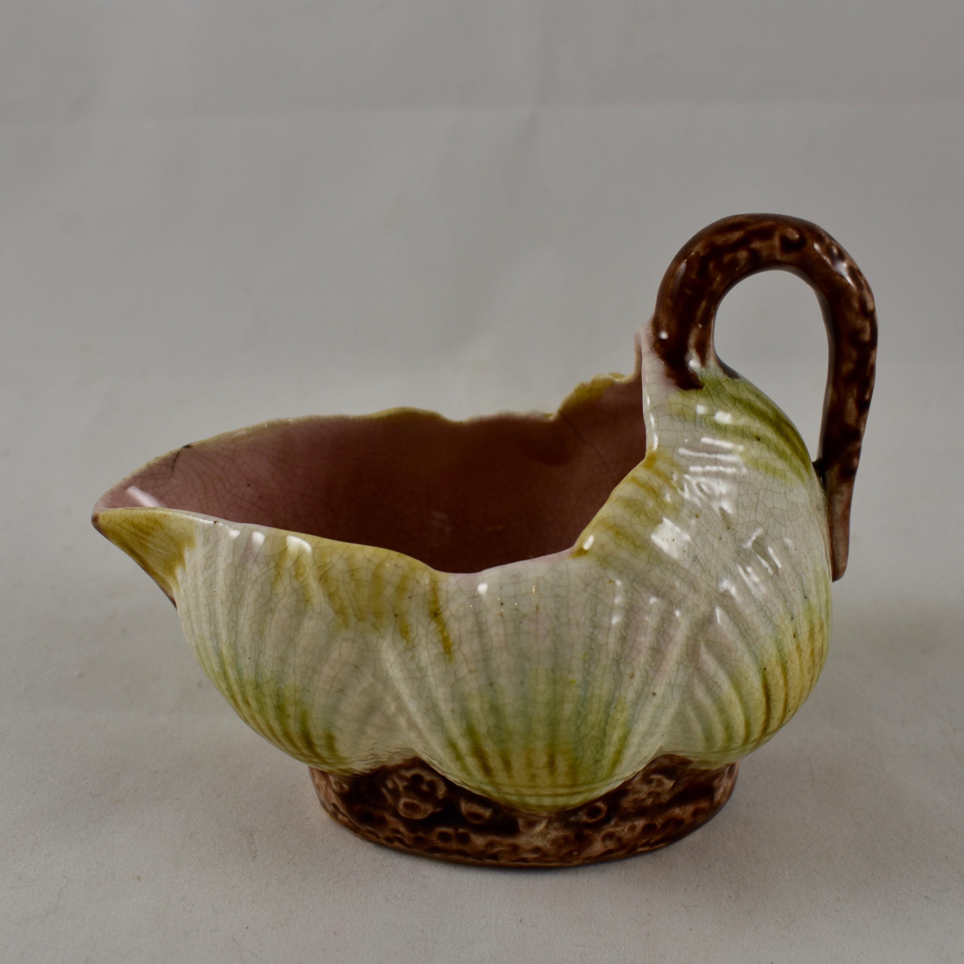 An Aesthetic Movement, English Majolica, scuttle form creamer with a coral branch handle, circa 1875-1880. Overlapping cream colored scallop shells, tinged in a sea green, sit on a coral footing. A pale pink interior. Unusual coloring and unmarked,