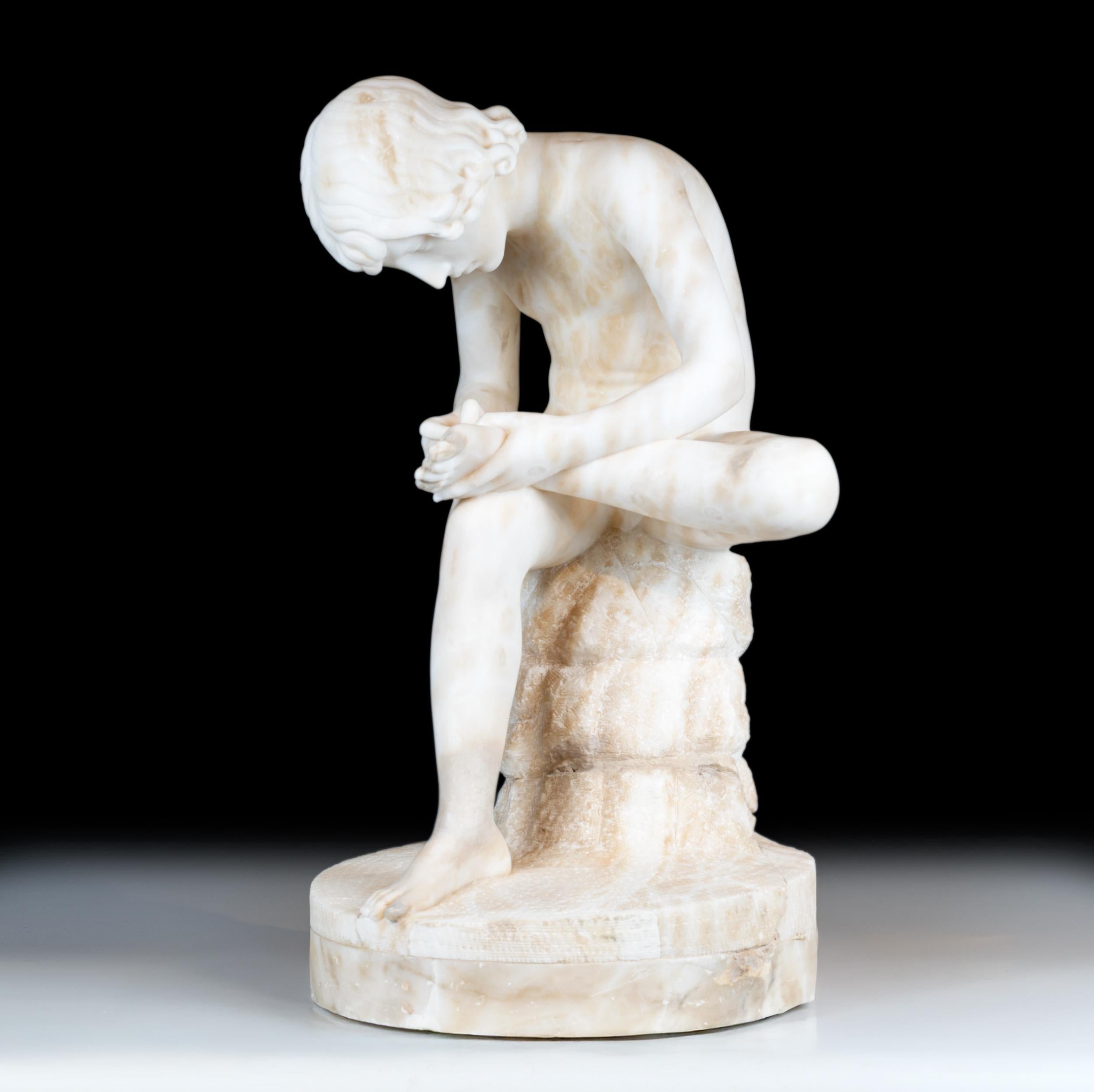 A well-executed alabaster figure of a nude boy seated on a rocky base, leaning forward intently as he removes a thorn from his foot. The carving demonstrates fine anatomical detailing and a sensitive portrayal of youthful concentration. The base is