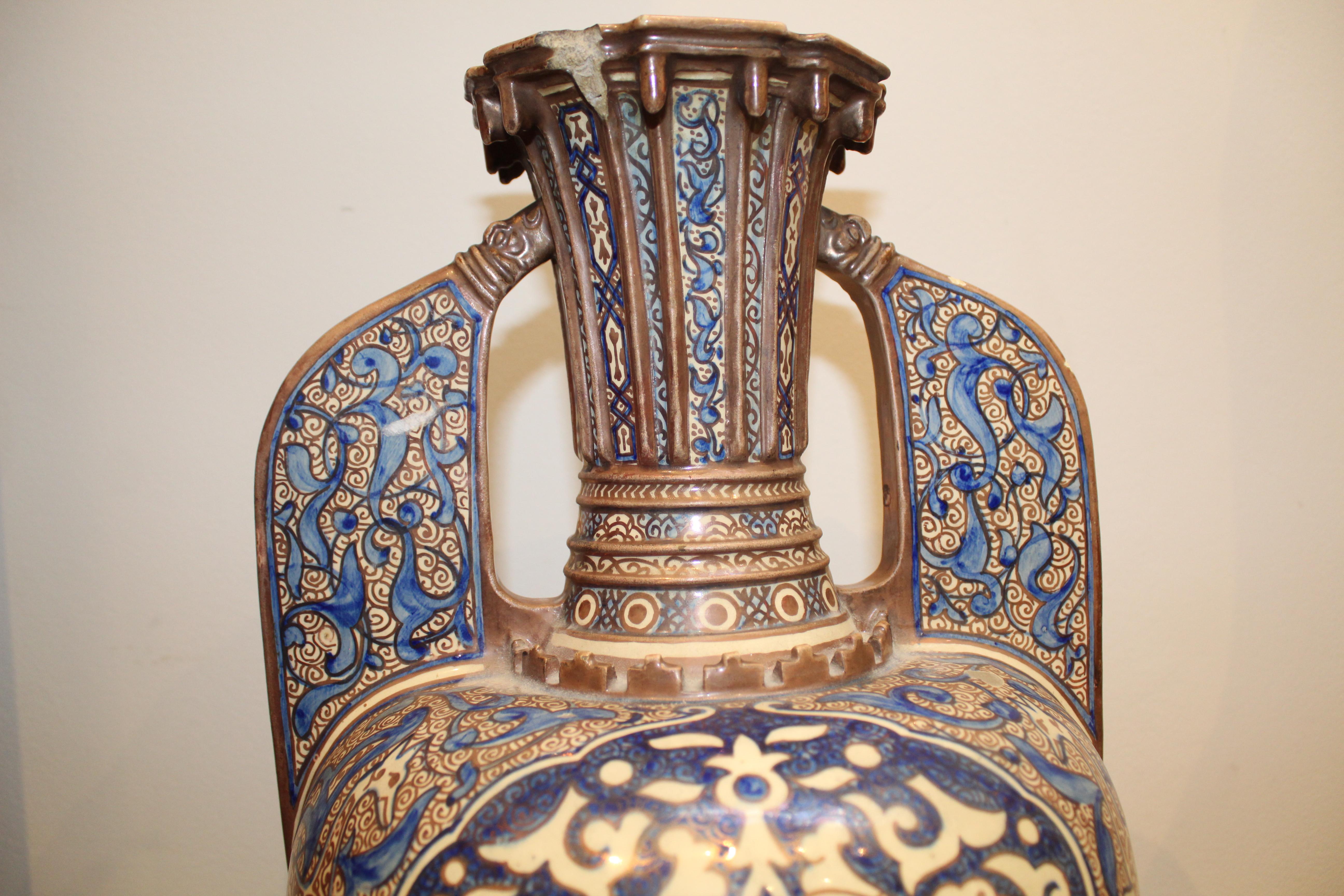 With a pear-shaped body and two 'wing' handles connected to the tall neck. It features various colours in decoration, such as blue, gold, and white. Made in Spain for the Islamic market.

Measures: With stand: height 63cm 
Width: 30cm.