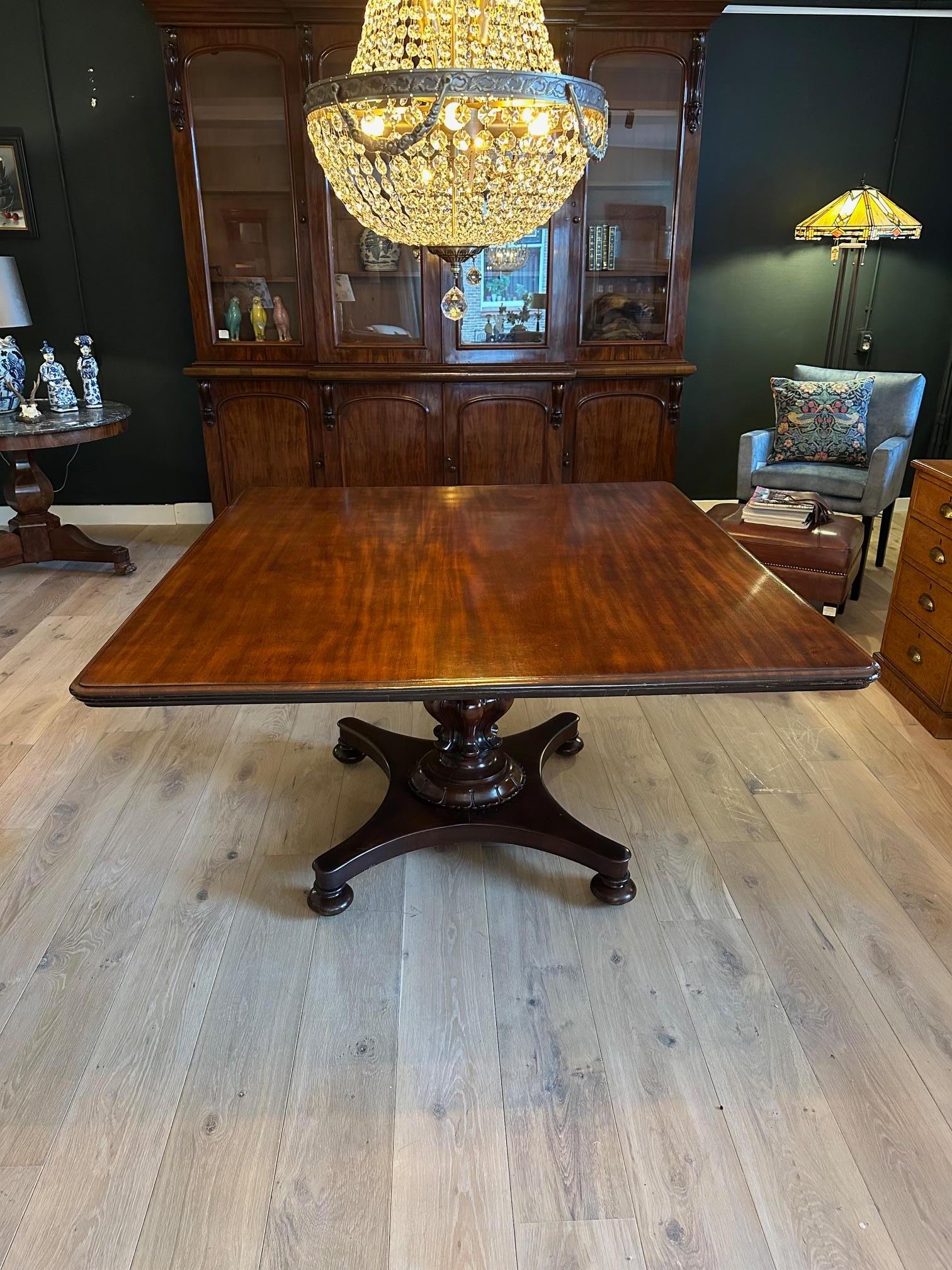 Magnifique table de salle à manger ancienne en acajou, presque carrée. La table a une belle base en forme de colonne sculptée. Le dessus a une belle patine. Cette table peut accueillir plus de 6 personnes. Grâce à son pied central, il convient