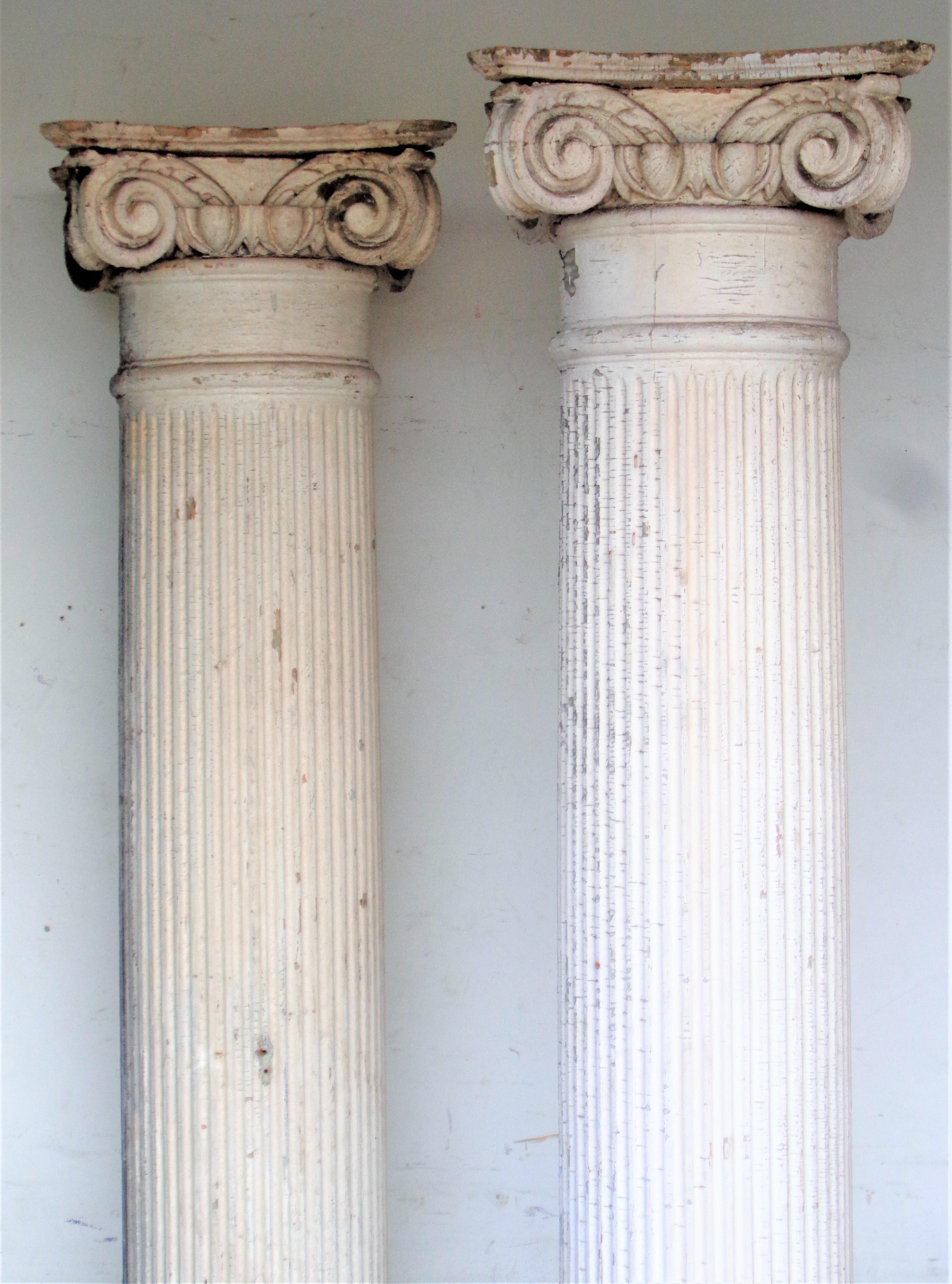 A good pair of antique 19th century American architectural fluted wood columns w/ carved wood Ionic capitals in nicely aged original antique condition w/ old worn soft white painted surface. Columns measure 79 inches high x 12 inches across column x