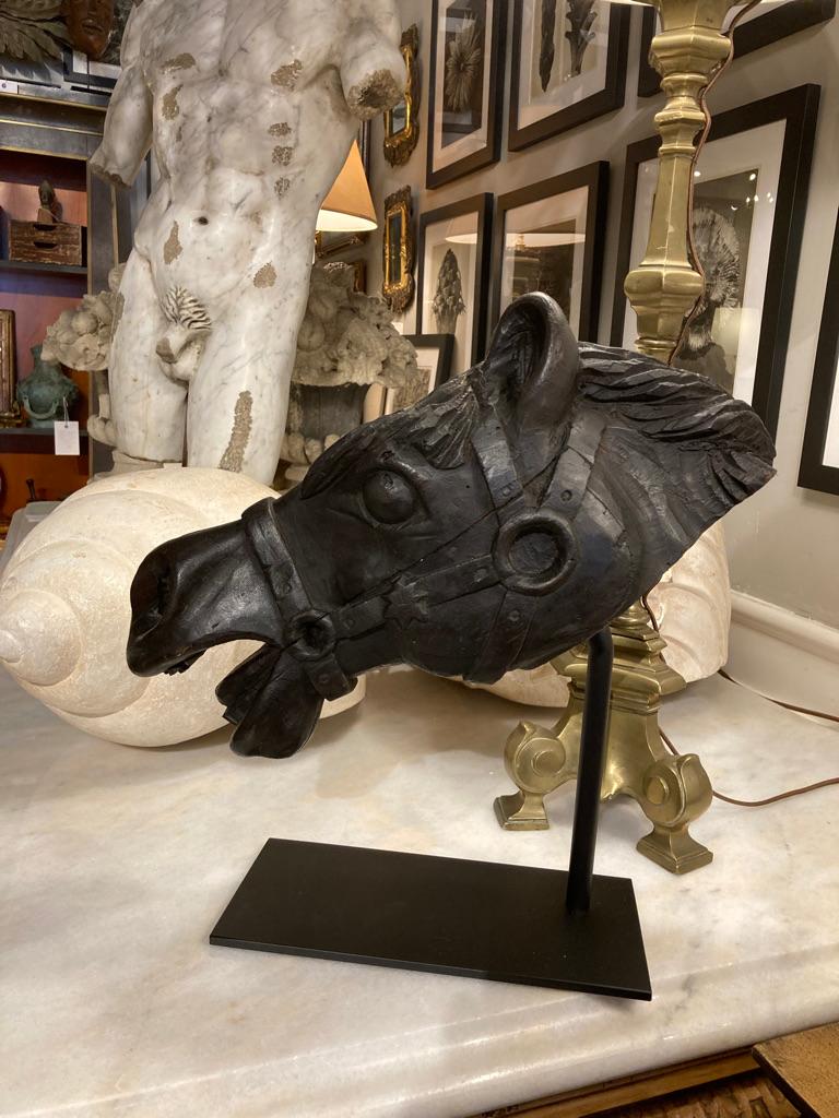 Hand carved wood head of a horse, stained black, shown wearing a bridal and bit, with mouth open as if in a full gallop. A very handsome piece of sculpture, likely a fragment from a larger piece, now mounted on a custom iron base. Great decoration