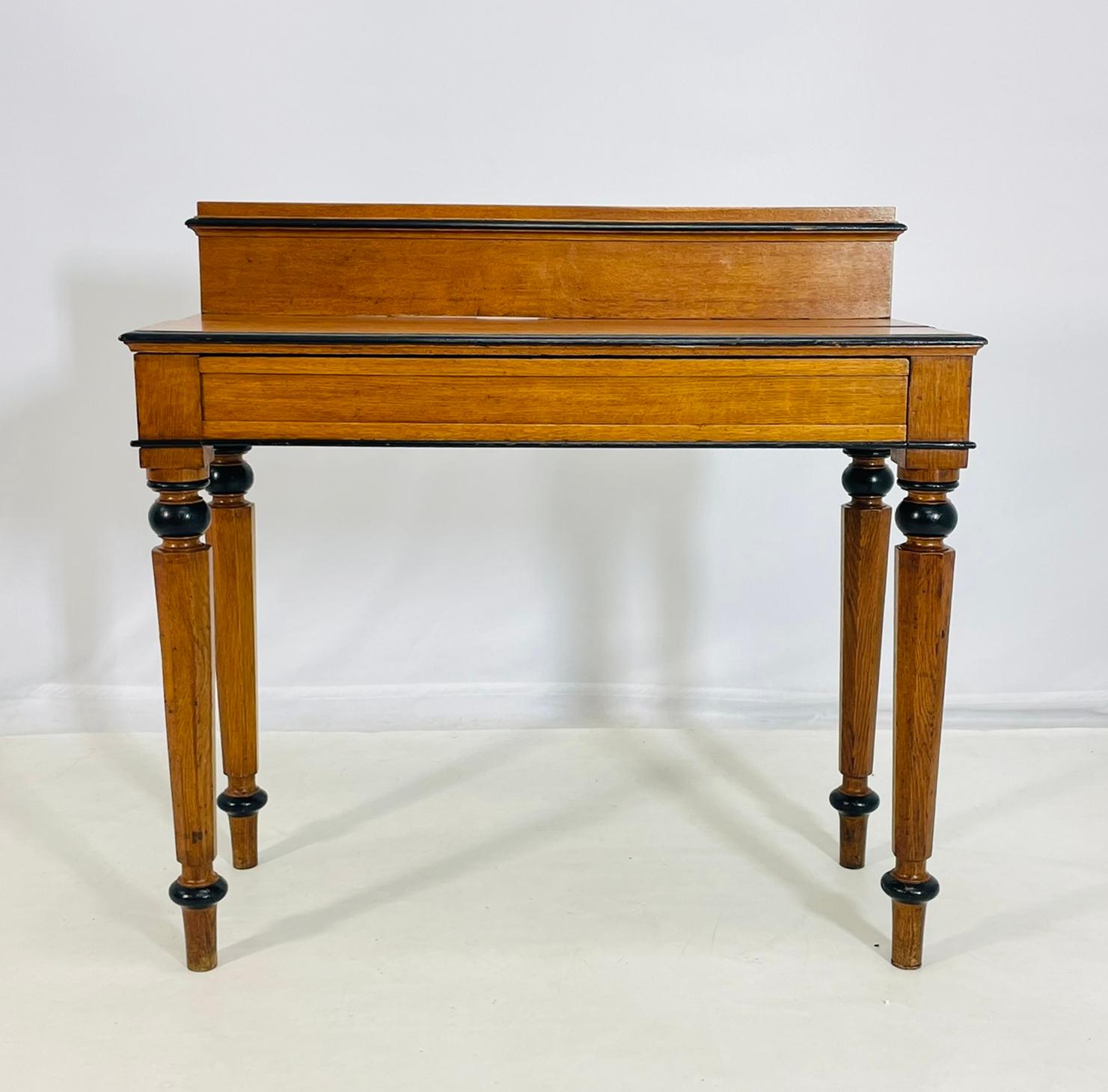 A beautifully crafted late 19th century American writing table in the Classical Revival style, featuring elegant turned legs and refined contrasting details. Made of solid oak, the table showcases a warm honey-toned finish highlighted by ebonized