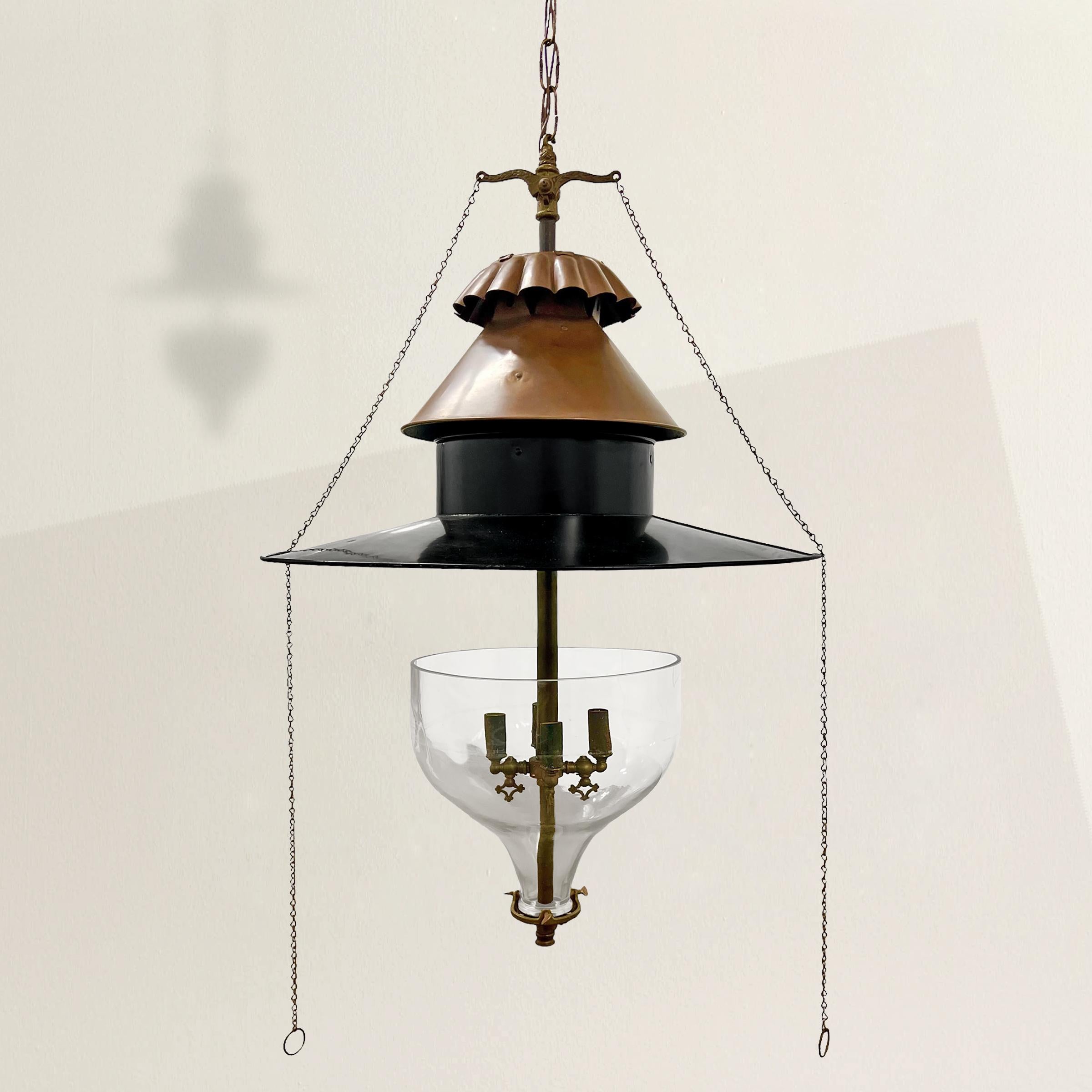 Radiating 19th-century charm, this American oil lamp chandelier, now fully electrified, is a testament to timeless design and innovation. Its large round copper and steel shade exudes historic elegance, while four lights suspended in an inverted