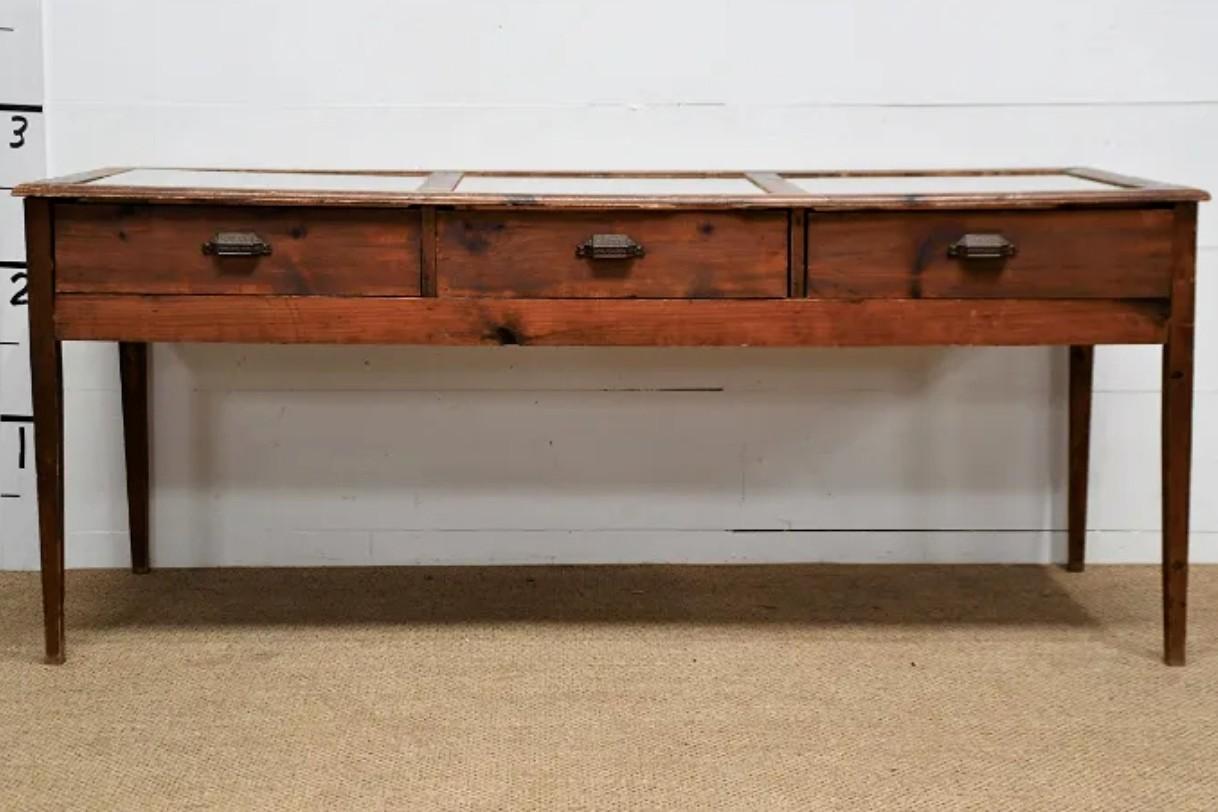 A rare antique American country general store haberdashery display showcase table. 19th century, wood and glass, having a rectangular top inset with three glass panels, over three drawers affixed with metal pulls, rising on squared tapered legs.