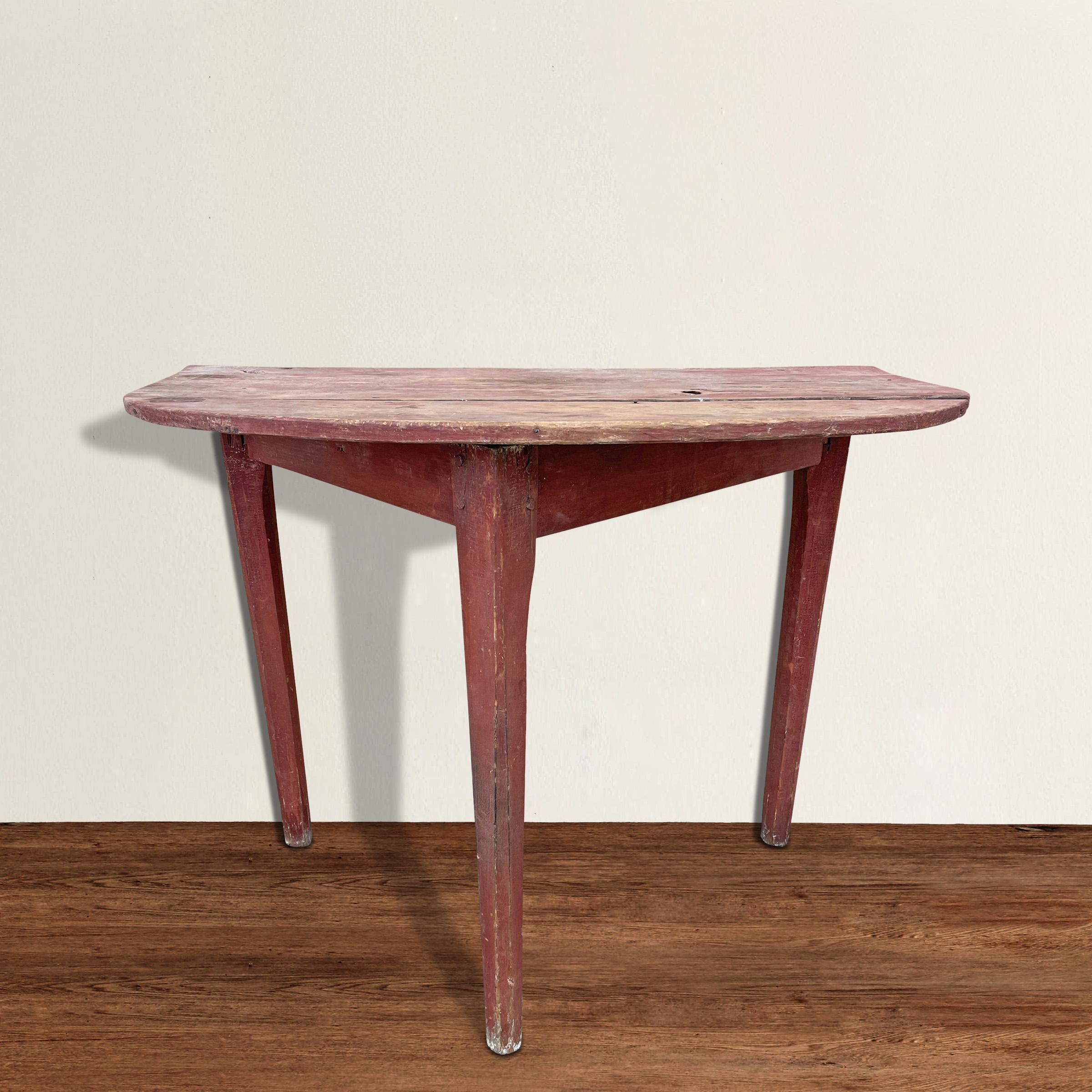 A charming 19th century American pine demilune table with three tapered and chamfered legs with wooden pegs, asymmetrically positioned, and retaining its original red paint. The top is semi-circular with squared off ends. Please note that the center