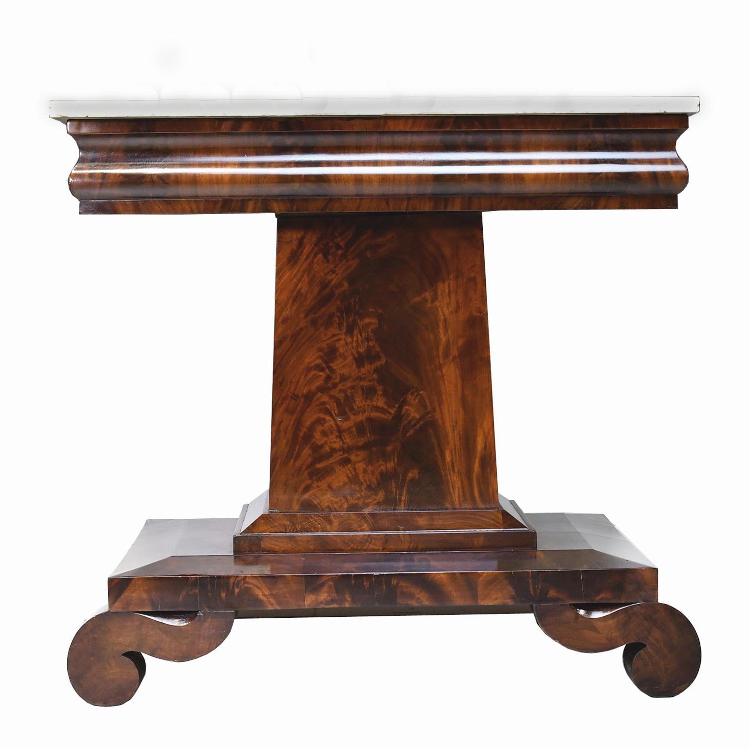 A handsome Empire console table in Fine West Indies mahogany in the Grecian style with square column resting on a beveled base with scroll feet, and original white Carrara marble top, New York City, circa 1820. In the school of Joseph