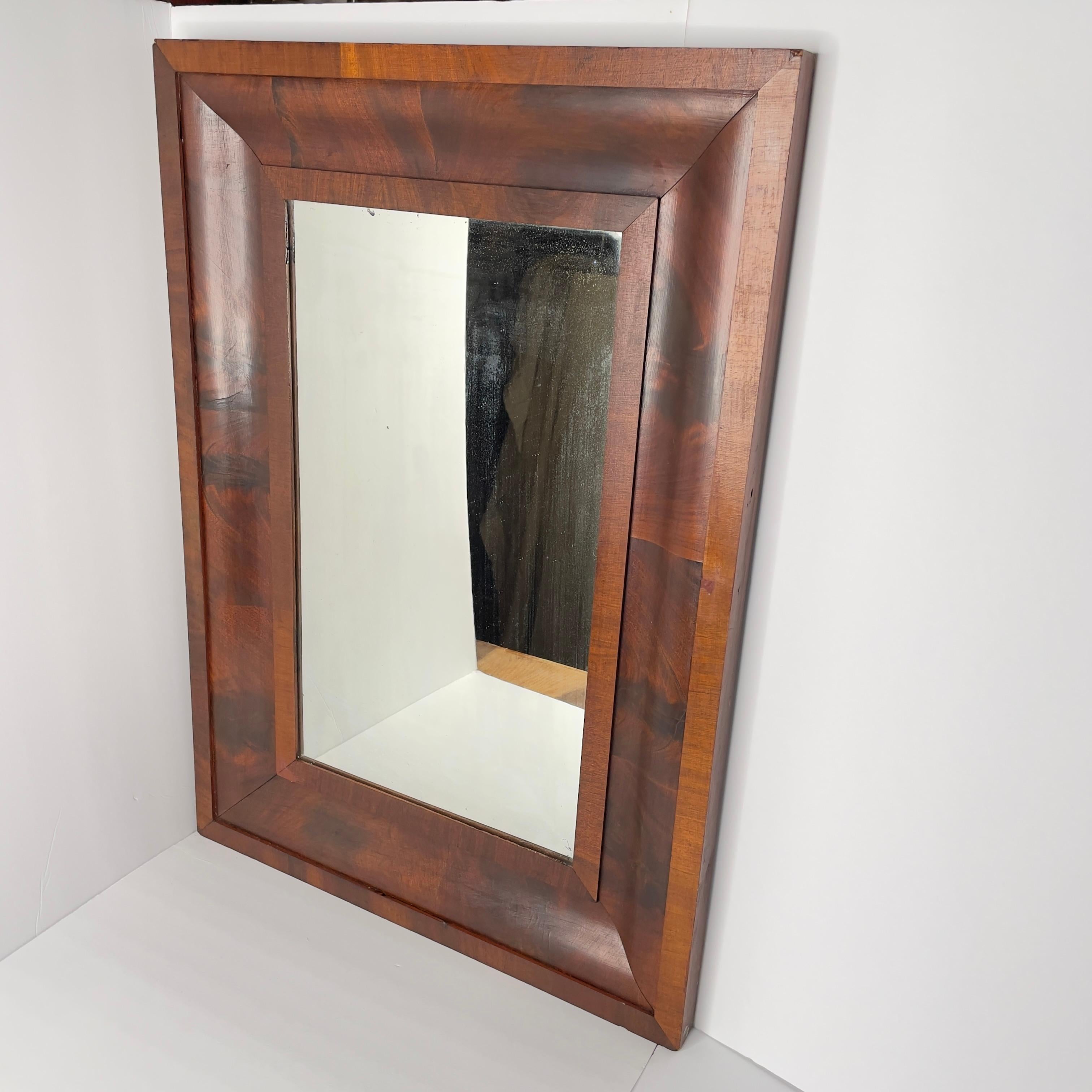 Antique 19th Century flame mahogany wall mirror with a solid wood backing. The mirror is wired to be hung on the wall, the wide ways. If you prefer the other direction, that can easily be accomplished with some new hardware and wire. 

The mirror