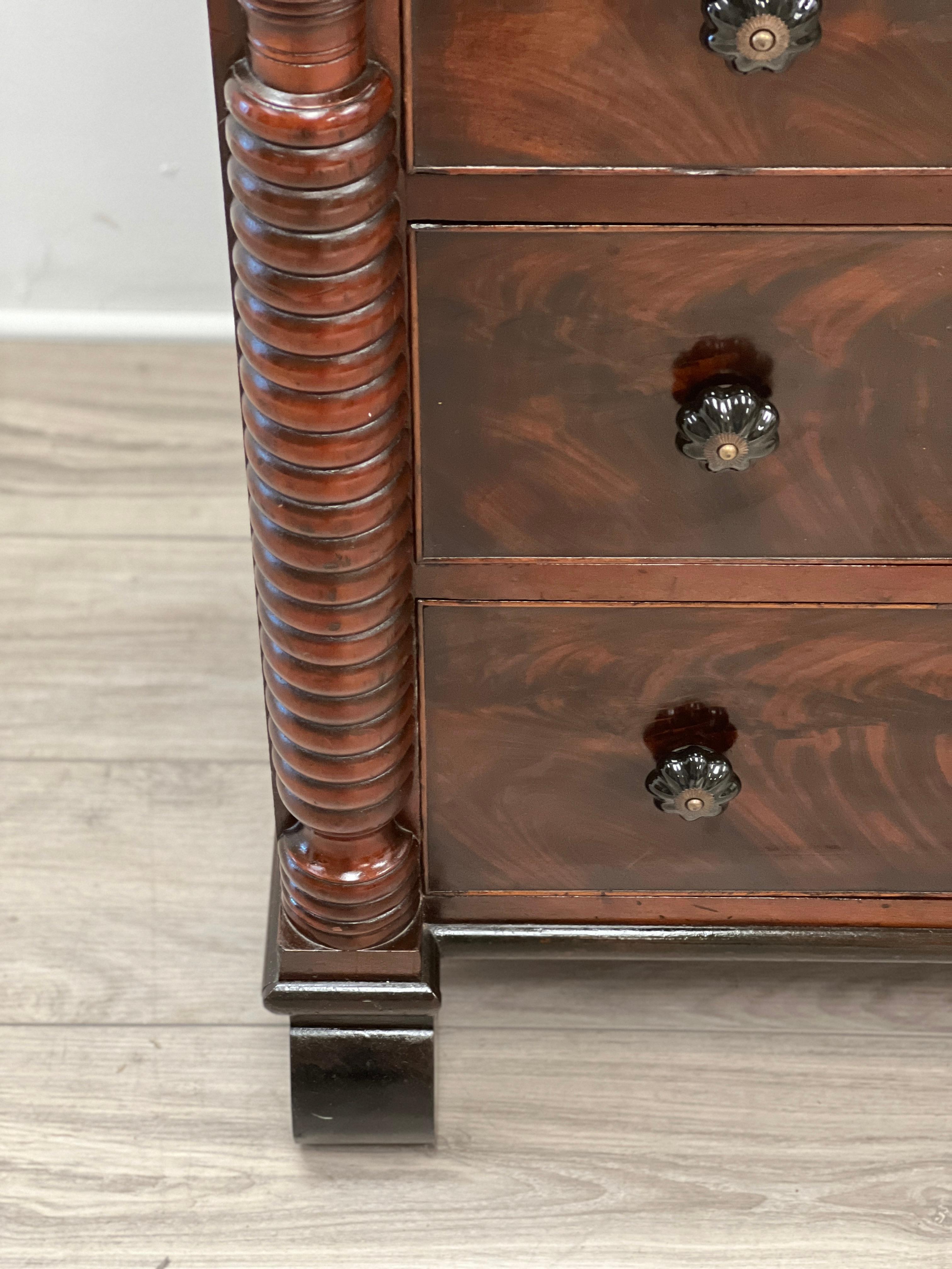 Featured is a very handsome American Empire chest of drawers built from gorgeous flamed crotched mahogany. This is four drawers built with hand cut dovetails. Each drawer is fitted with black glass pulls that were added at a later date. This chest