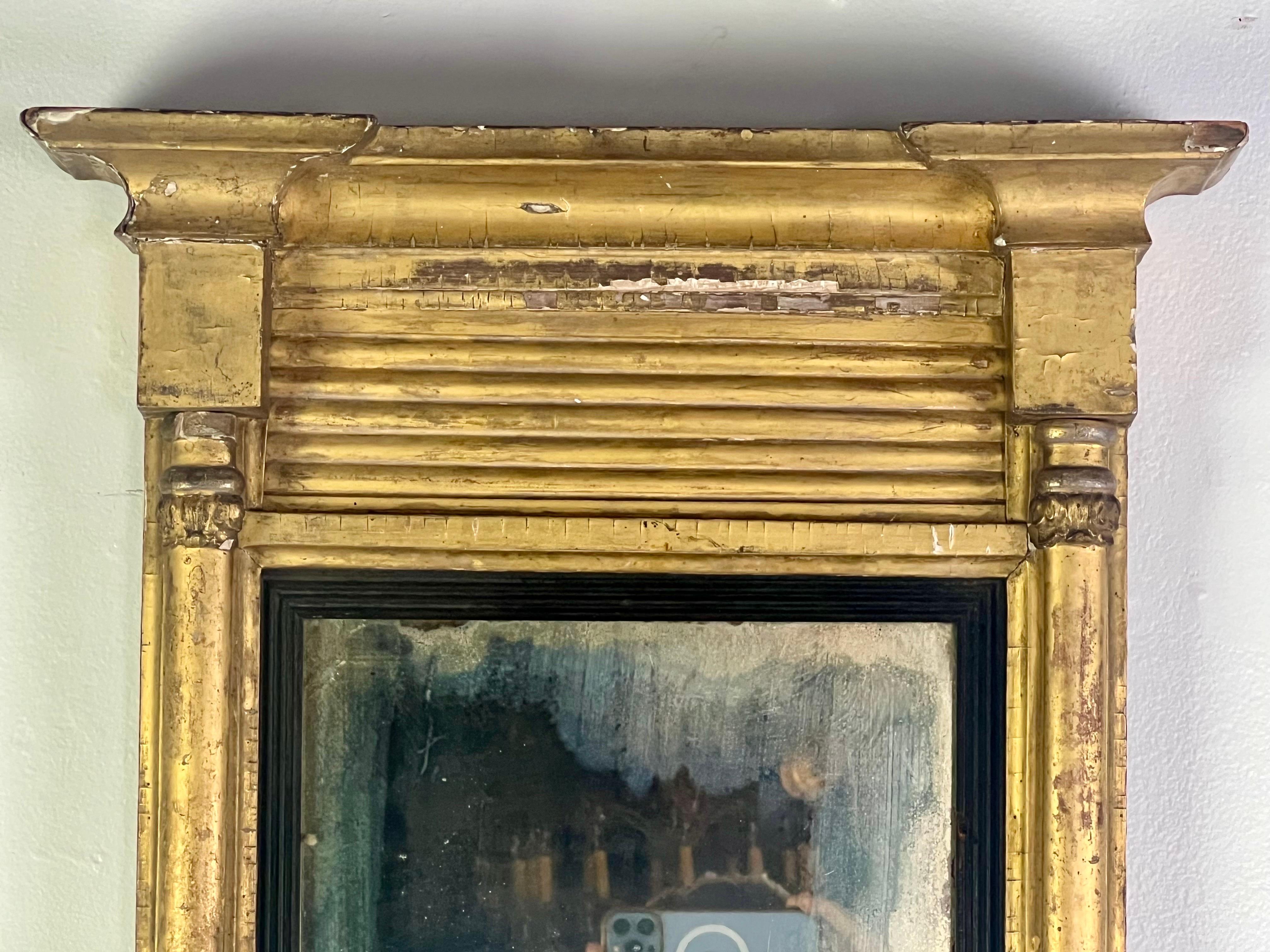 A 19-century American Empire Style gilt-wood mirror, designed in a rectangular shape with an antiqued mirror insert, is a classic and elegant piece that would bring a touch of timeless beauty to any space.