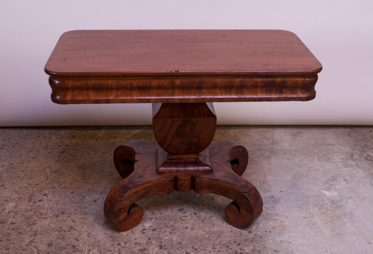 American Empire parlor table, circa late 1800s. Surface is supported by a pedestal base with scroll feet. Impressive mahogany burl grain and rich tone. 
Conservative restoration was employed to even the wood tone. Moderate, age-commensurate wear