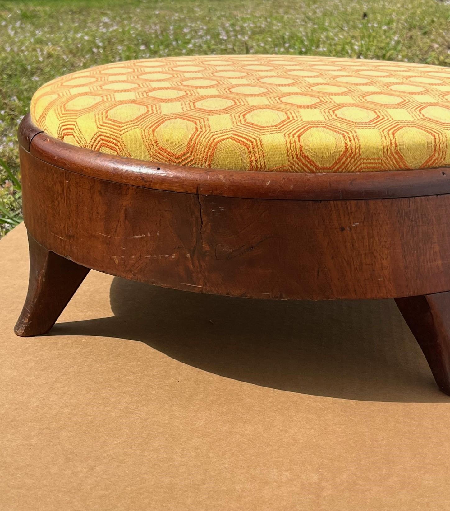 19th Century American Empire Round Upholstered Footstool.

Round, footed stool with rich mahogany wood veneer stands on four short, hand-carved, flared and graduated legs.  A great room accessory.
Condition is good antique.  Wear commensurate with