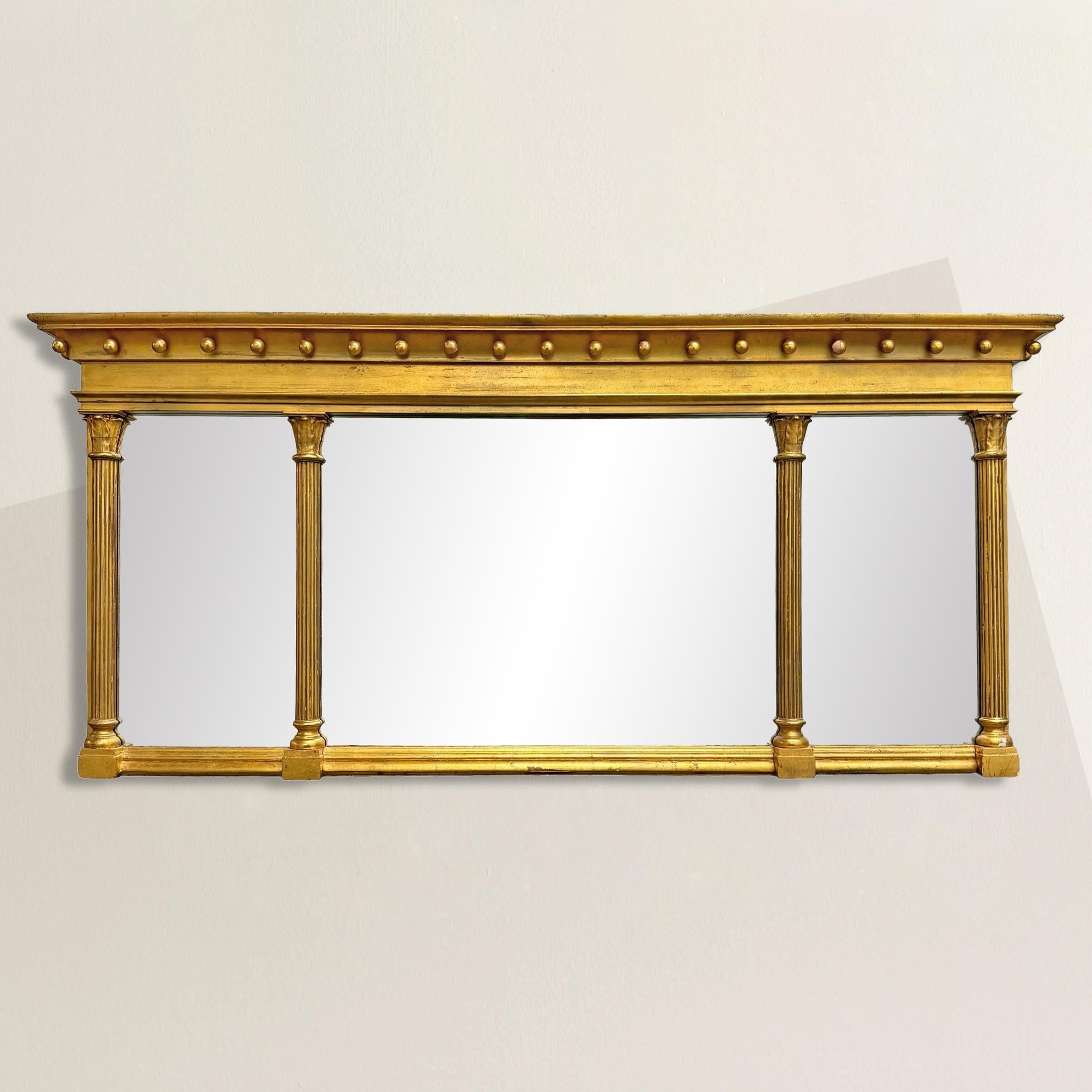 This 19th Century American Federal style gilt wood mirror is a quintessential example of the elegance and symmetry that define the Federal design aesthetic. Its frame, adorned with stylized Corinthian columns, supports an entablature crowned with a